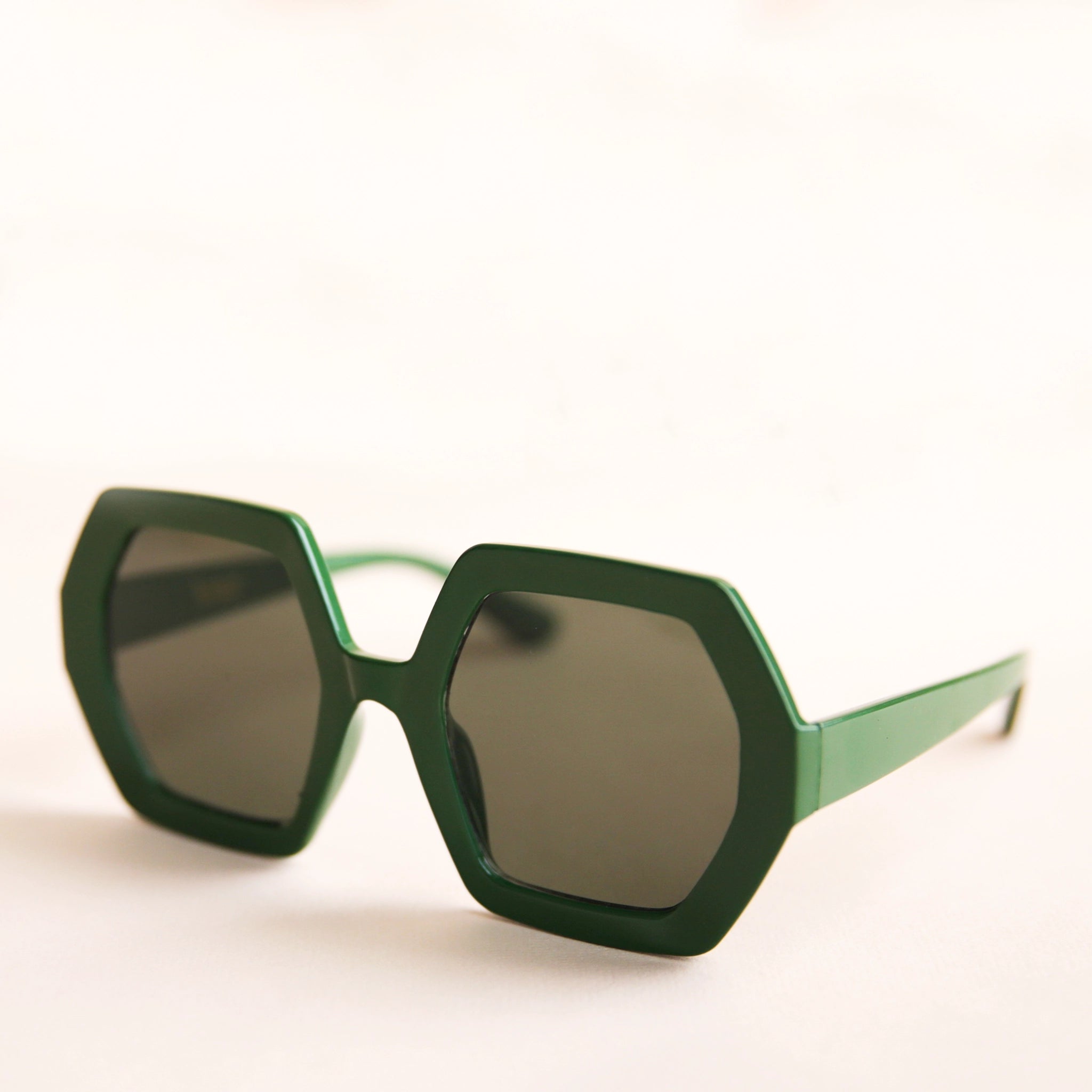 On a neutral background is a pair of hexagon shaped sunglasses in an emerald green color.