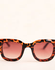 On a white background is a square pair of sunglasses with a brown and black tortoise pattern and a light brown lens.