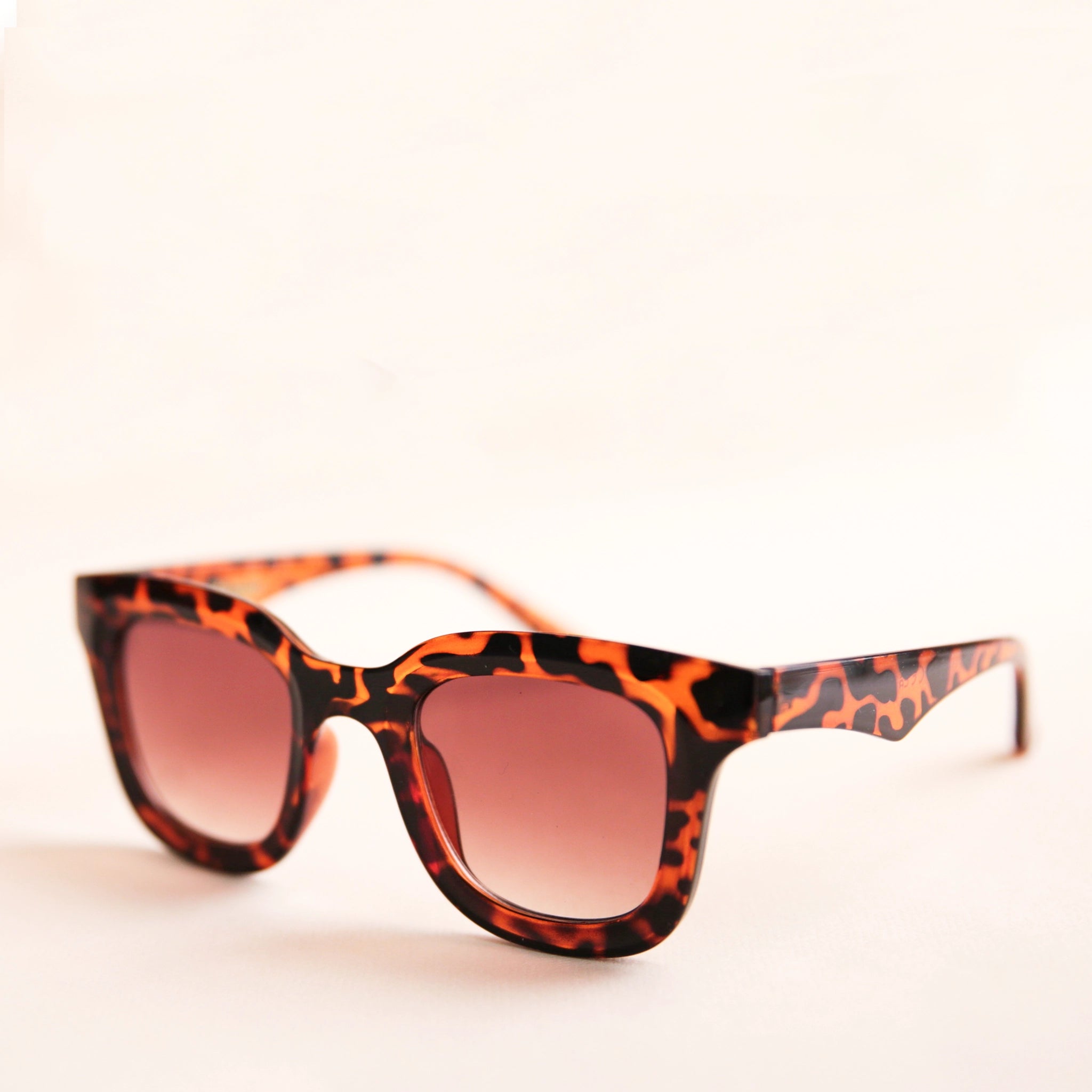 On a white background is a square pair of sunglasses with a brown and black tortoise pattern and a light brown lens. 