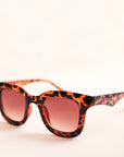 On a white background is a square pair of sunglasses with a brown and black tortoise pattern and a light brown lens. 