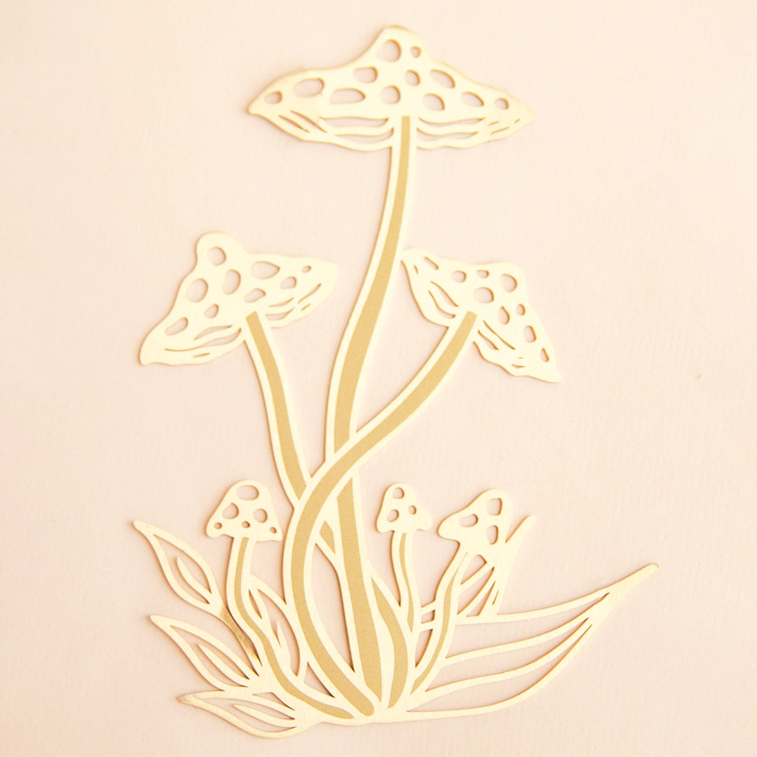 On a light pink background is a gold metal mushroom bookmark. 