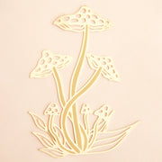 On a light pink background is a gold metal mushroom bookmark. 