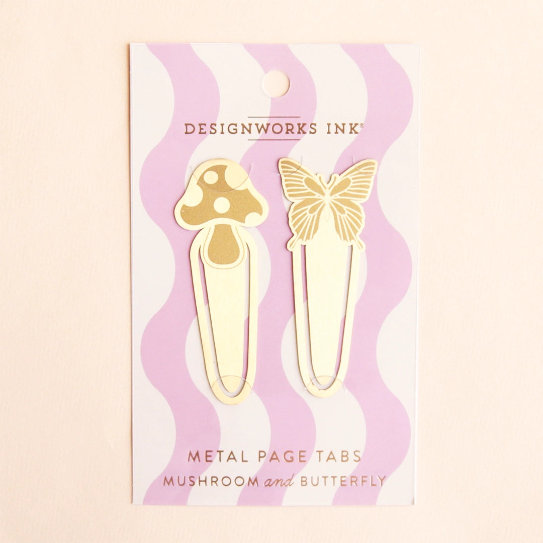 On a tan background is two gold book tabs one with a mushroom design and the other with a butterfly design and on a pink and white wavy cardboard packaging. 