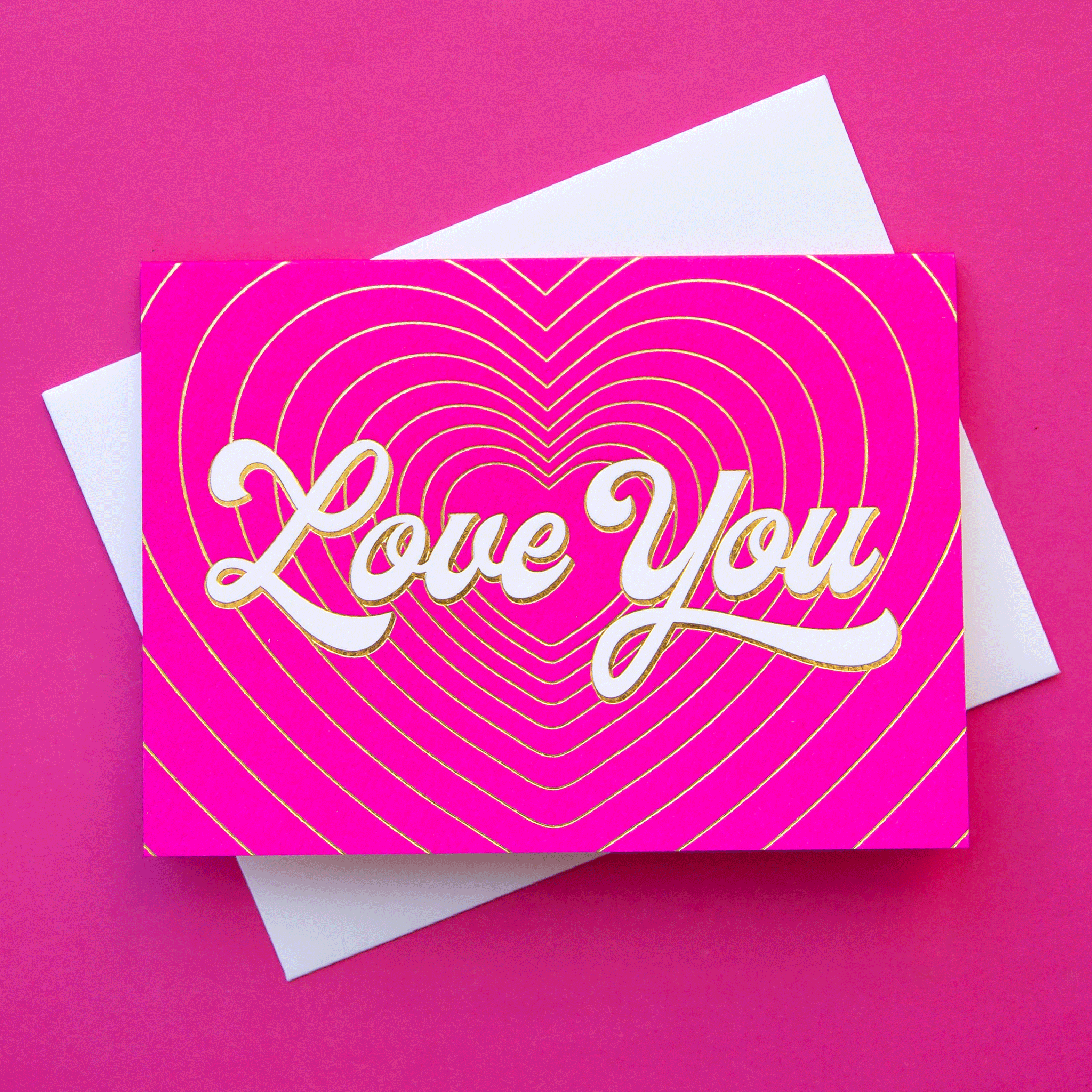 On a pink background is a hot pink card with gold heart shaped lines with ivory text in the center that reads, &quot;Love You&quot;.