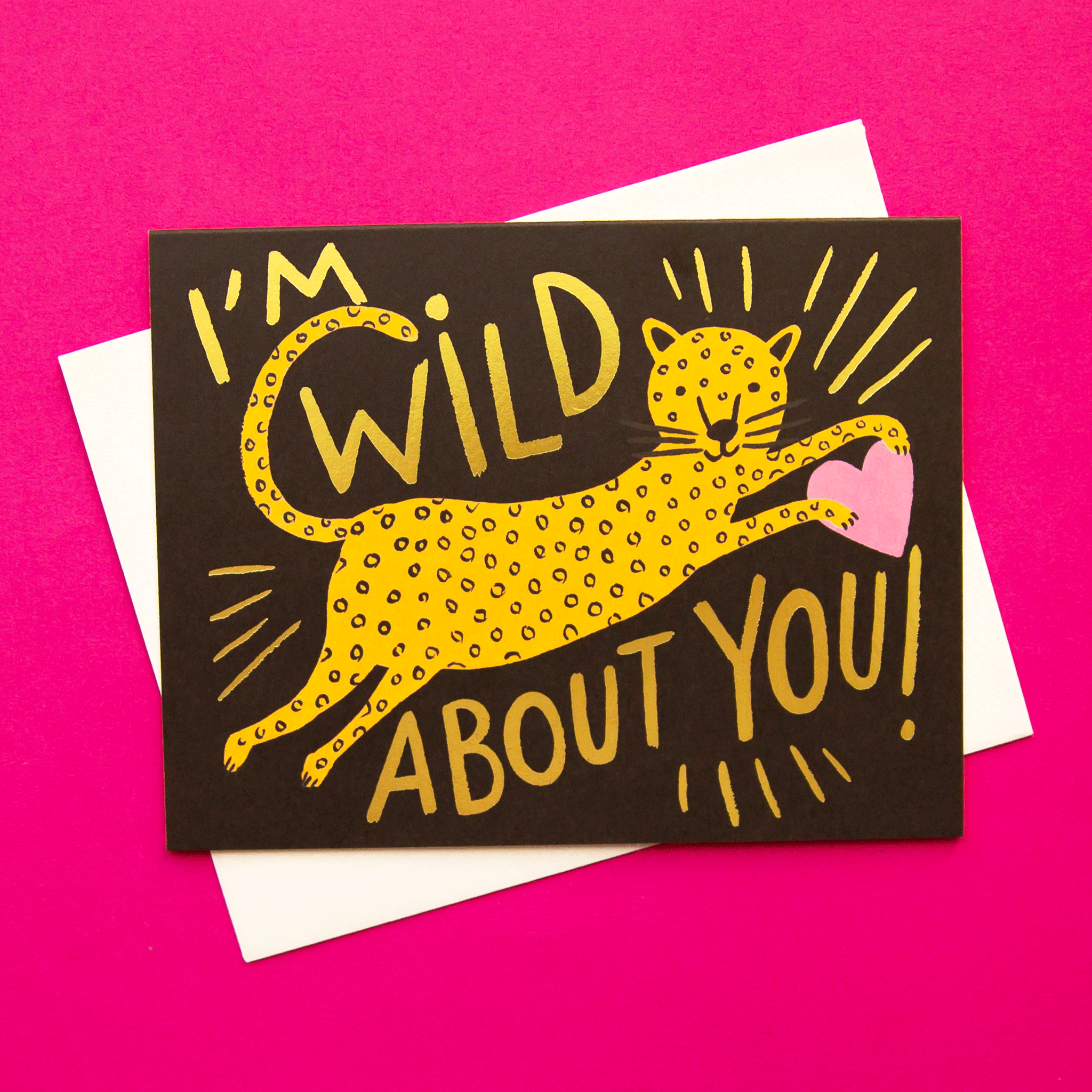 On a pink background is a black card with a leaping cheetah illustration holding a heart and gold text that reads, "I'm Wild About You".