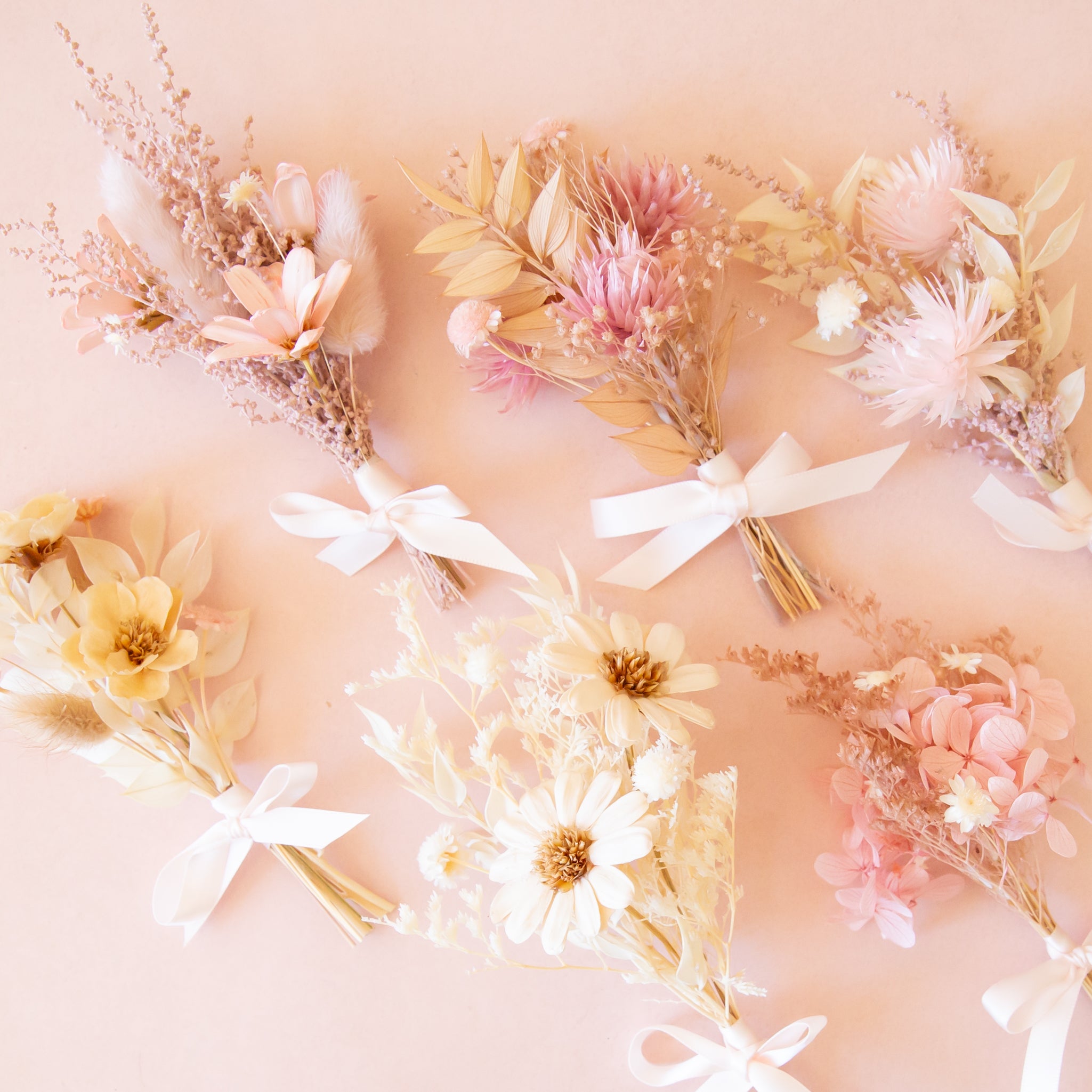 Eight pastel dried flower bouquets in soft pink, cream, and yellow are arranged in a loose grid on a pale peach background, each tied with a white ribbon.