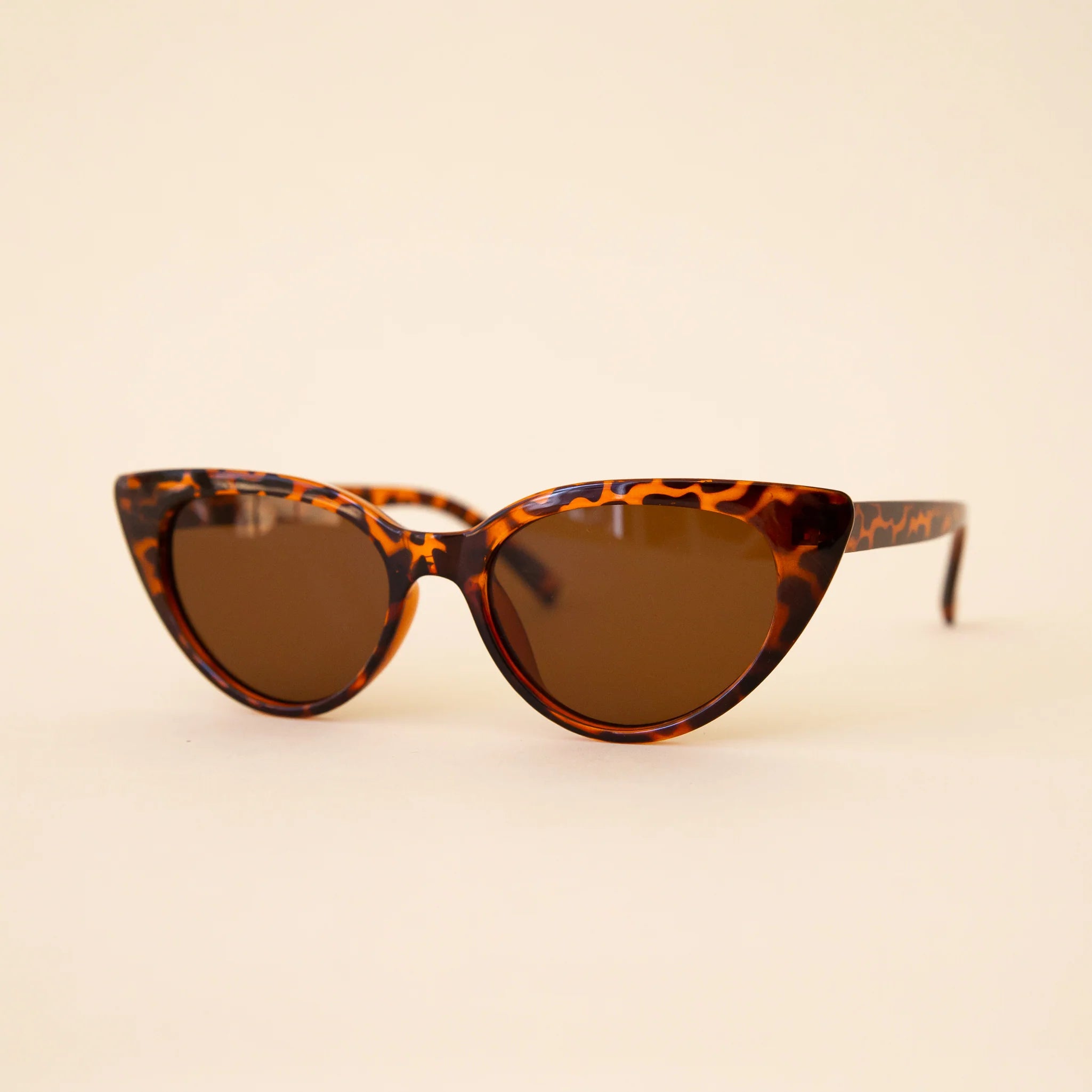 Tortoiseshell cat-eye sunglasses with brown lenses on a beige background