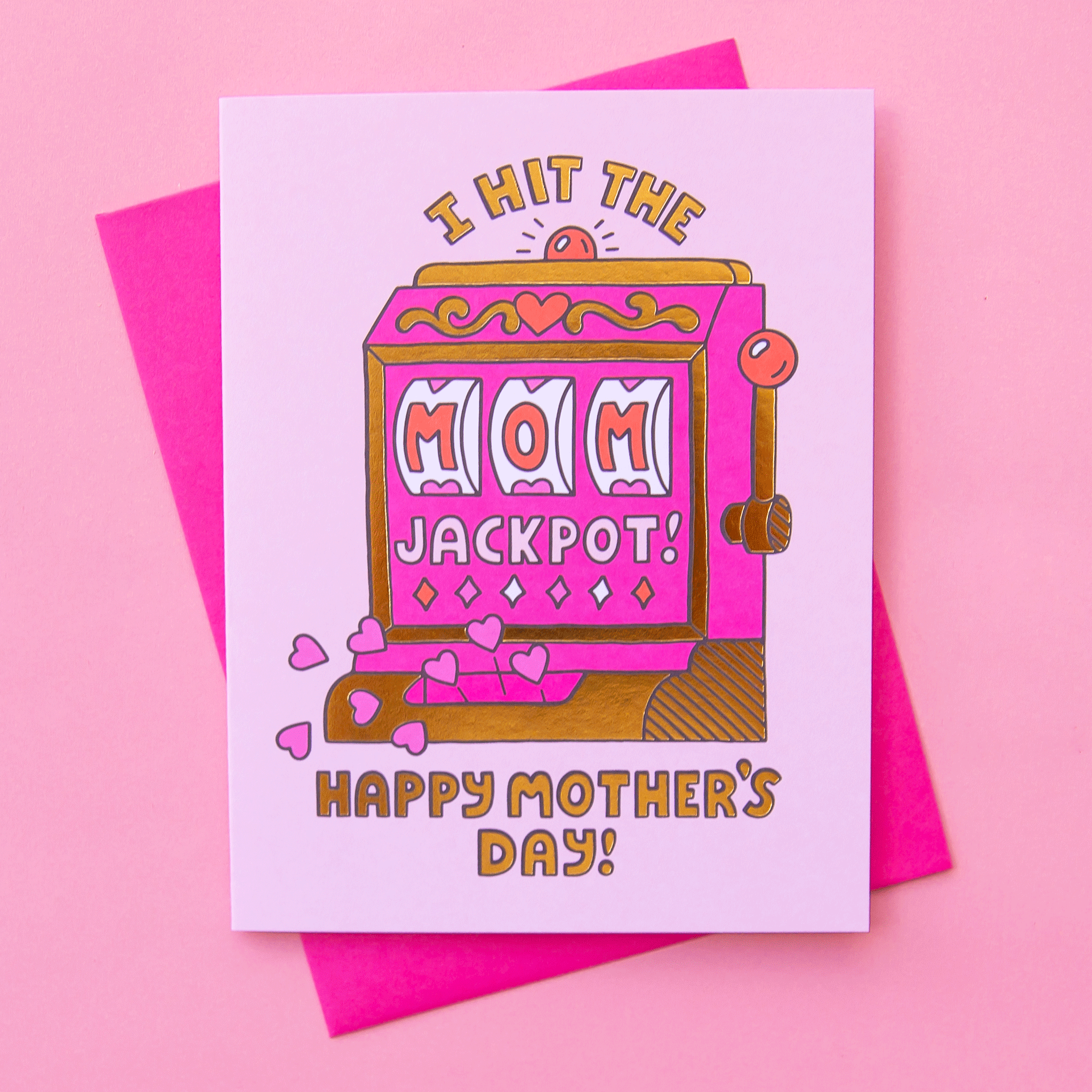 On a pink background is a white card with a pink and gold slot machine that's detailed with hearts and reads, "I hit the MOM jackpot! Happy Father's Day!". "MOM" is written in the slot machine as the winning numbers. Also included is a coordinating white envelope.