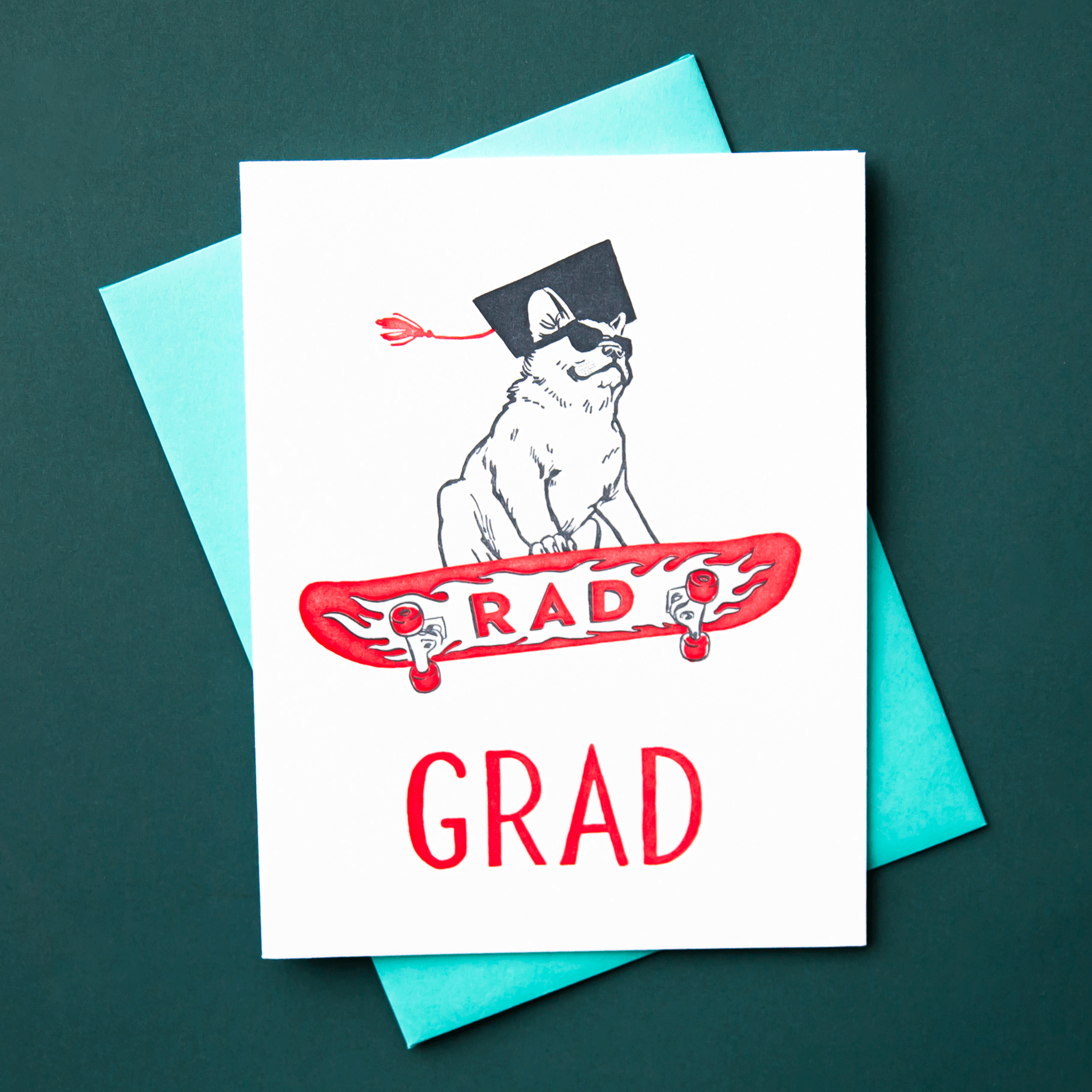 On a teal background is a ivory card with an illustration of a french bulldog on a skateboard that reads, "Rad Grad".