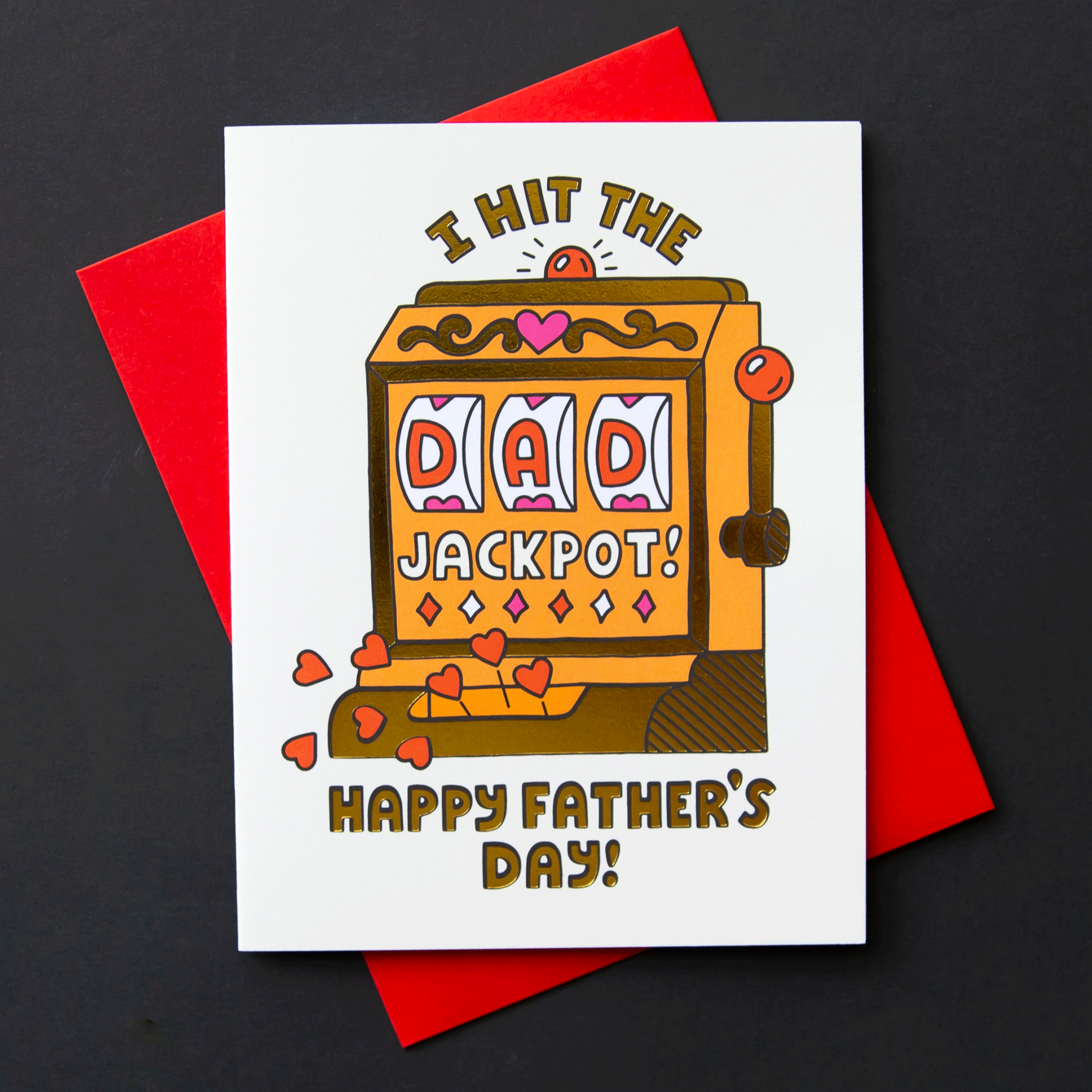 On a black background is a white card with an orange and gold slot machine that's detailed with hearts and reads, "I hit the DAD jackpot! Happy Father's Day!". "DAD" is written in the slot machine as the winning numbers. Also included is a coordinating white envelope.