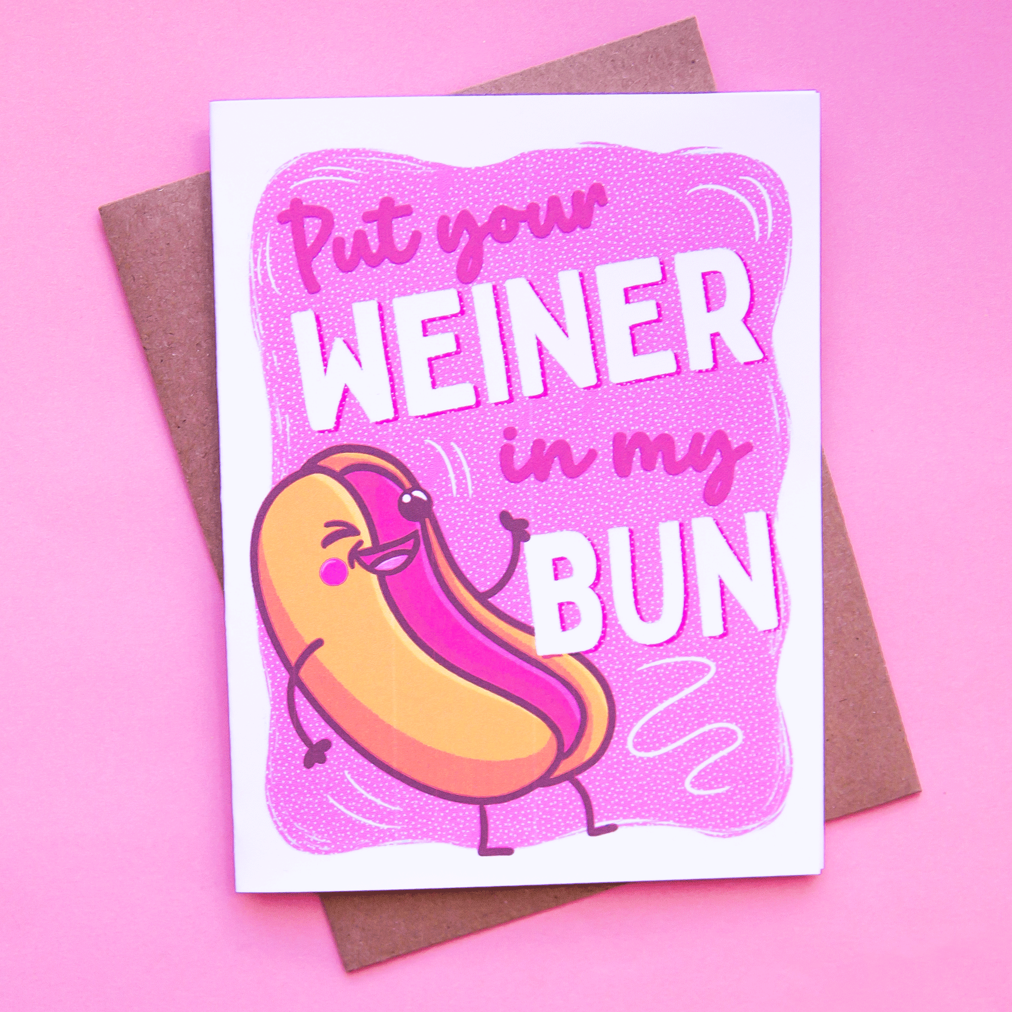 On a pink background is a pink card and a hot dog graphic with text that reads, &quot;Put your Weiner in my Bun&quot;.
