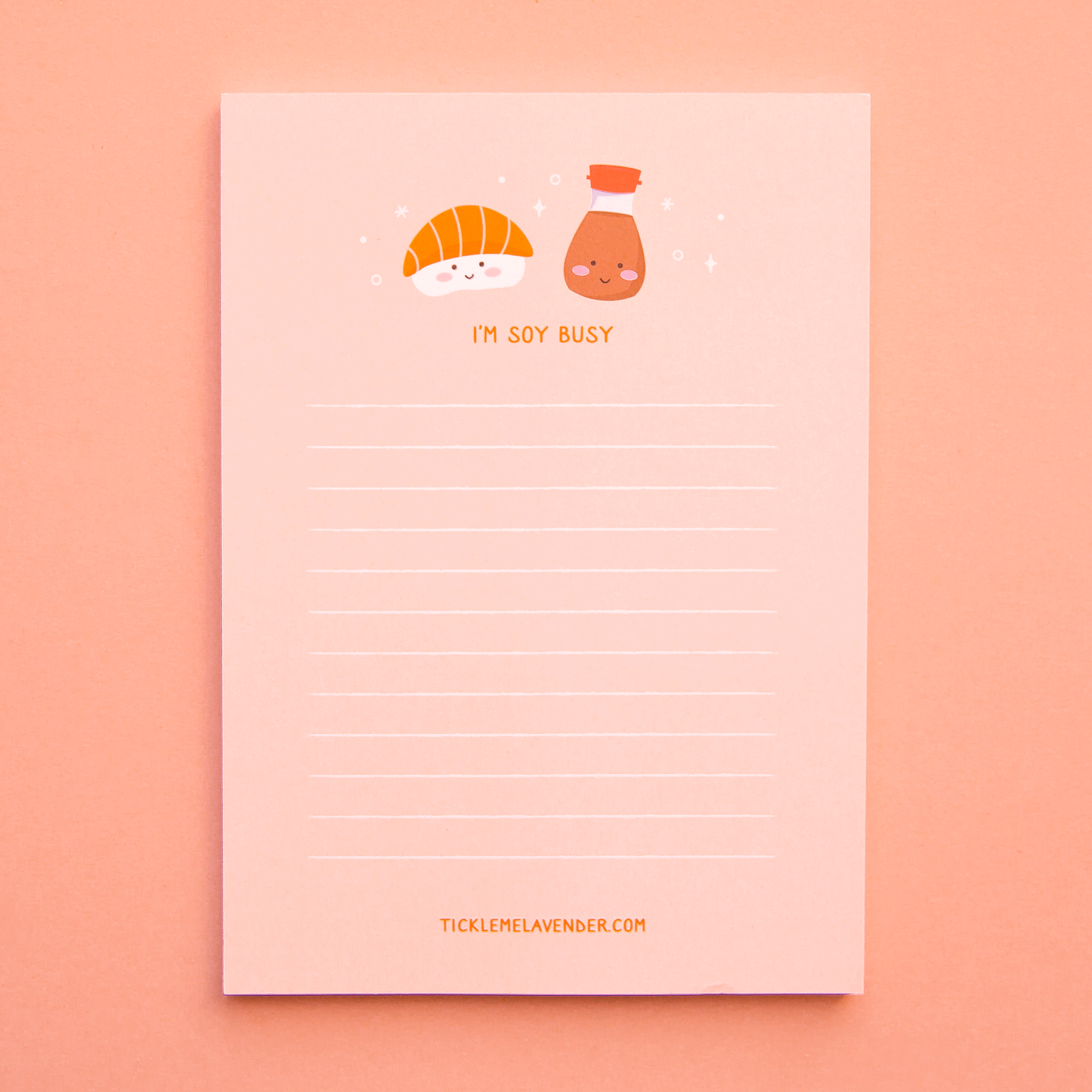 A light pink notepad with white lines for writing and a salmon sashimi and soy sauce graphic at the top along with orange letters underneath that read, "I'm Soy Busy".