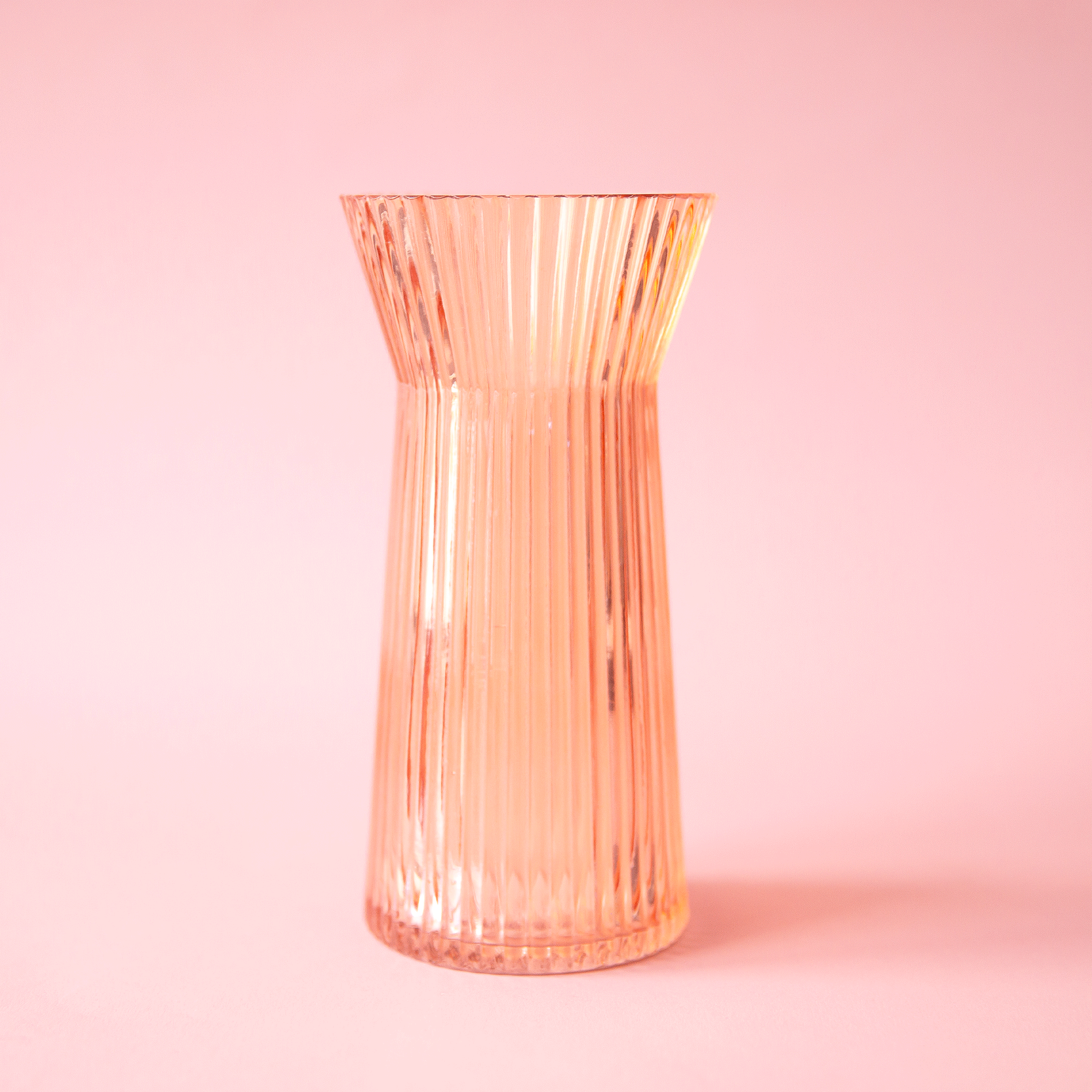 On a pink background is a apricot colored ribbed glass vase.