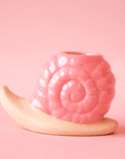 On a pink background is a pink snail shaped candle holder. 