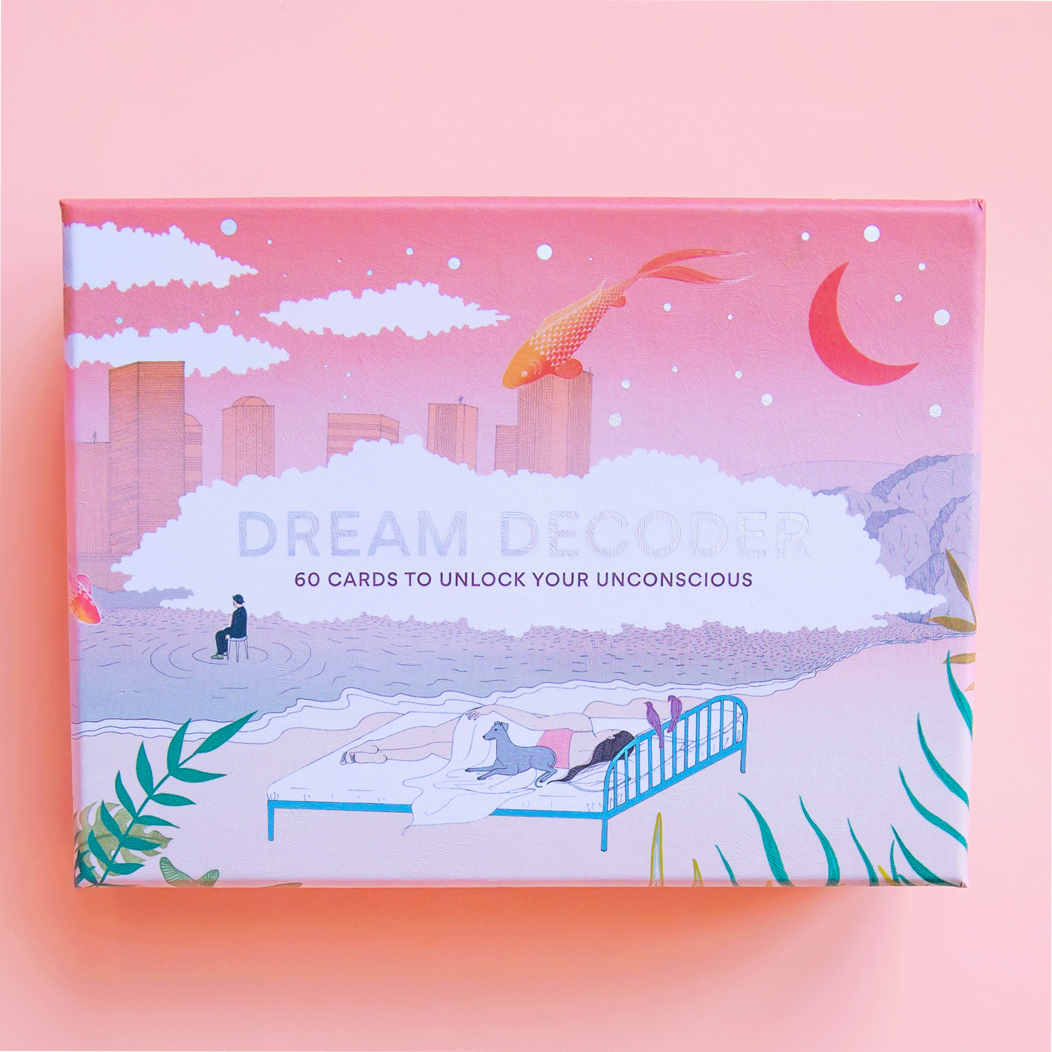 A box with dreamy graphics of the sky and a city with clouds and a bed on the beach. Also photographed are the cards inside of the box that have illustrations of different dream scenarios along with words on the back describing their meaning.