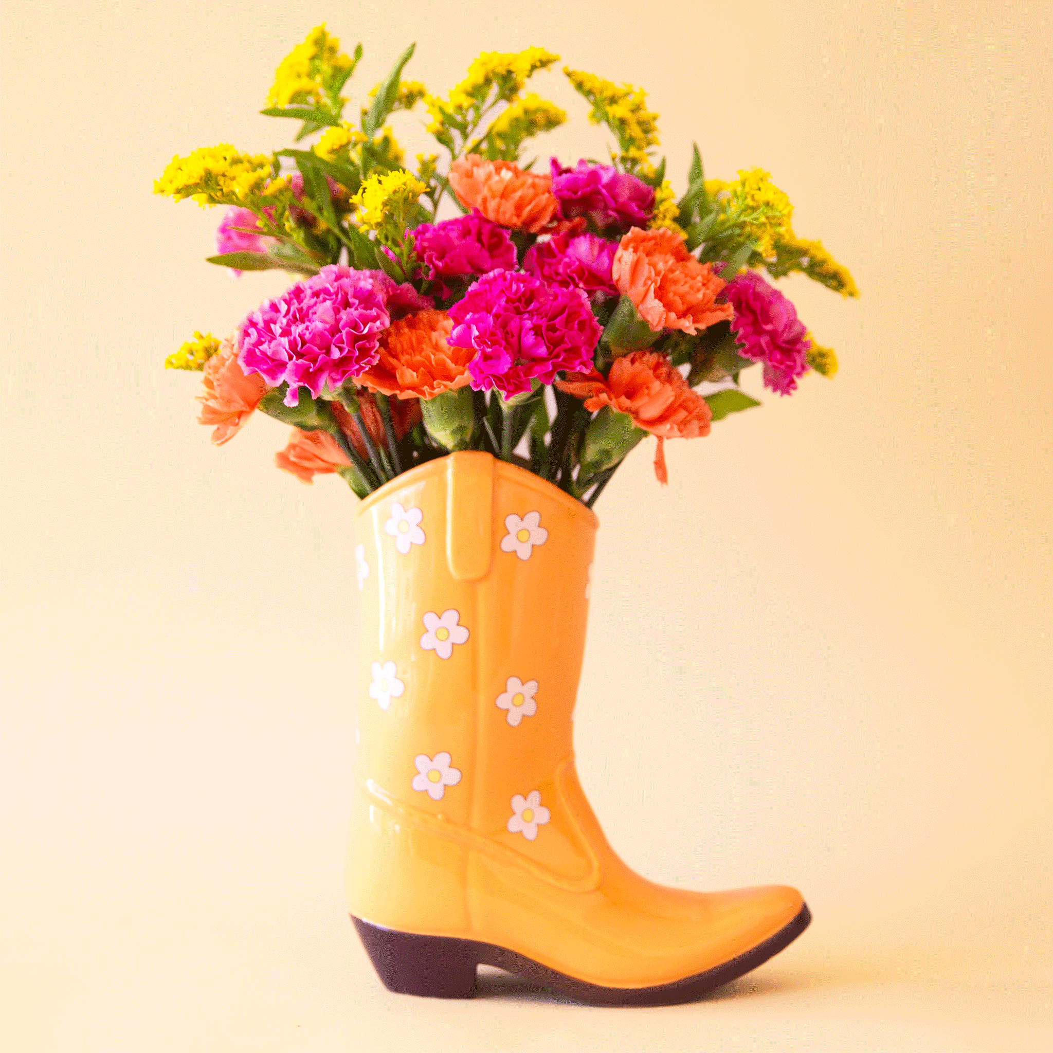 On a tan background is a yellow cowboy boot shaped vase with white and yellow daisy print all over. Flowers not included with purchase.