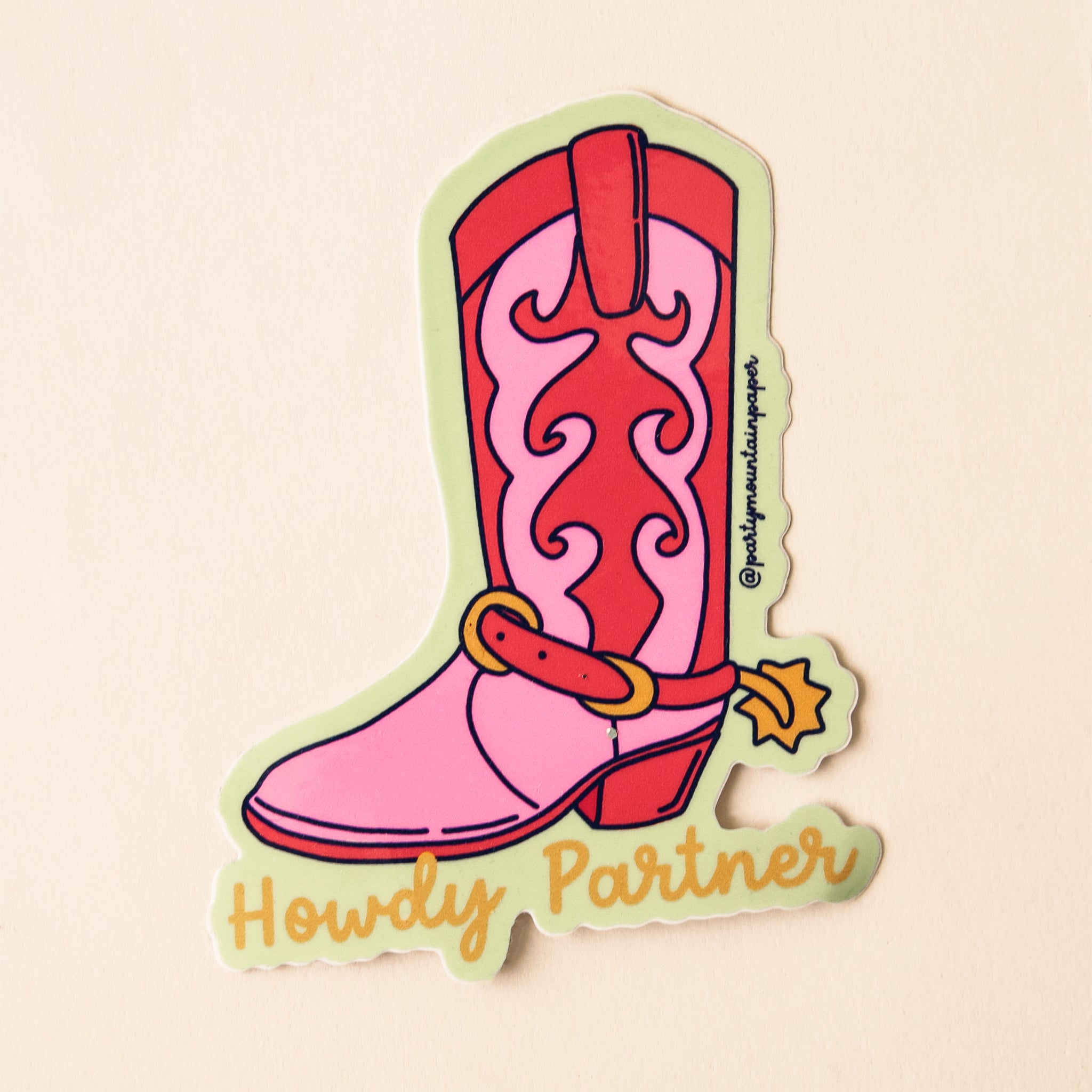 On a tan background is a red and pink cowgirl boot with yellow text at the bottom that reads, &quot;Howdy Partner&quot; in cursive font. 
