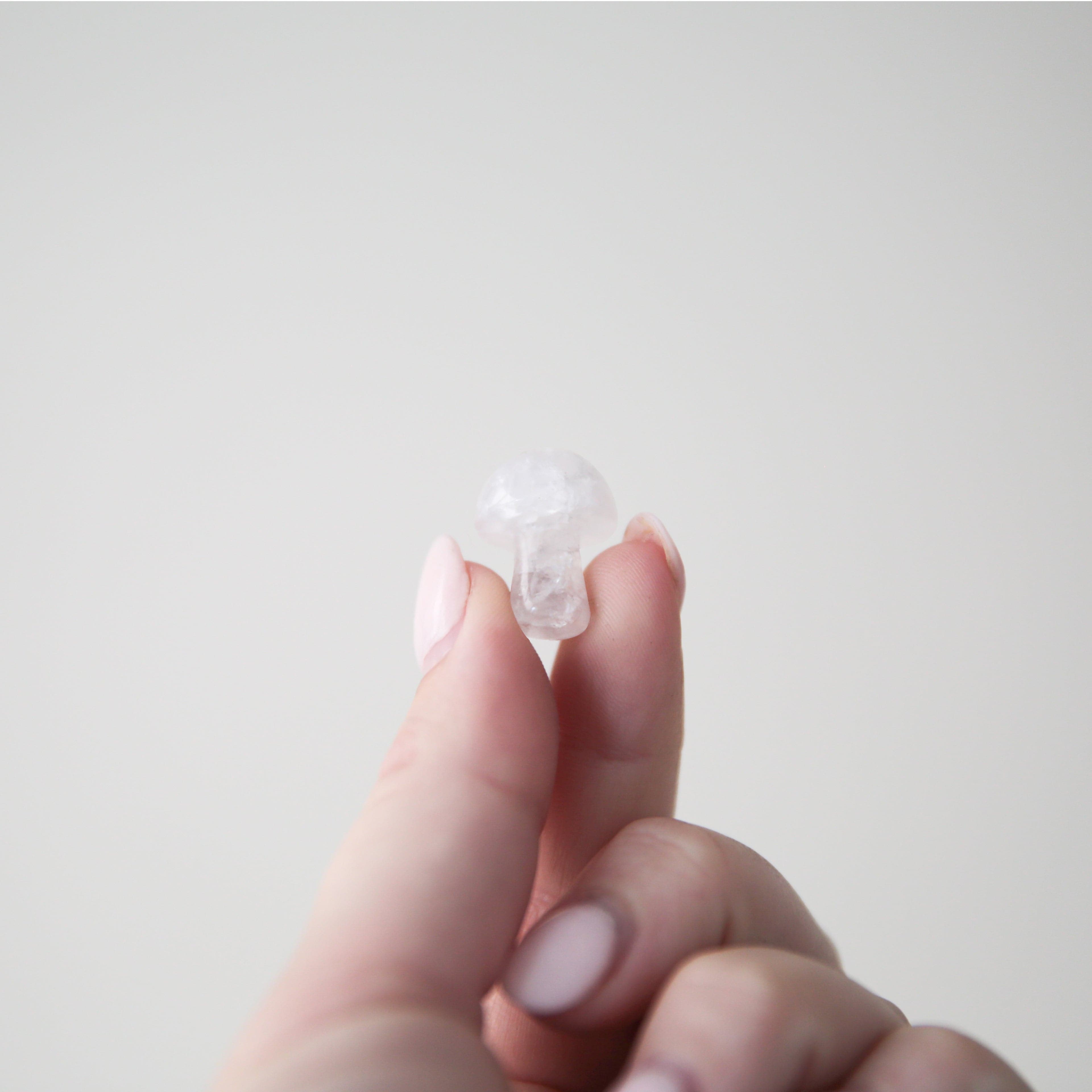 On a light gray background is a model holding a white quartz crystal in the shape of a tiny mushroom. 