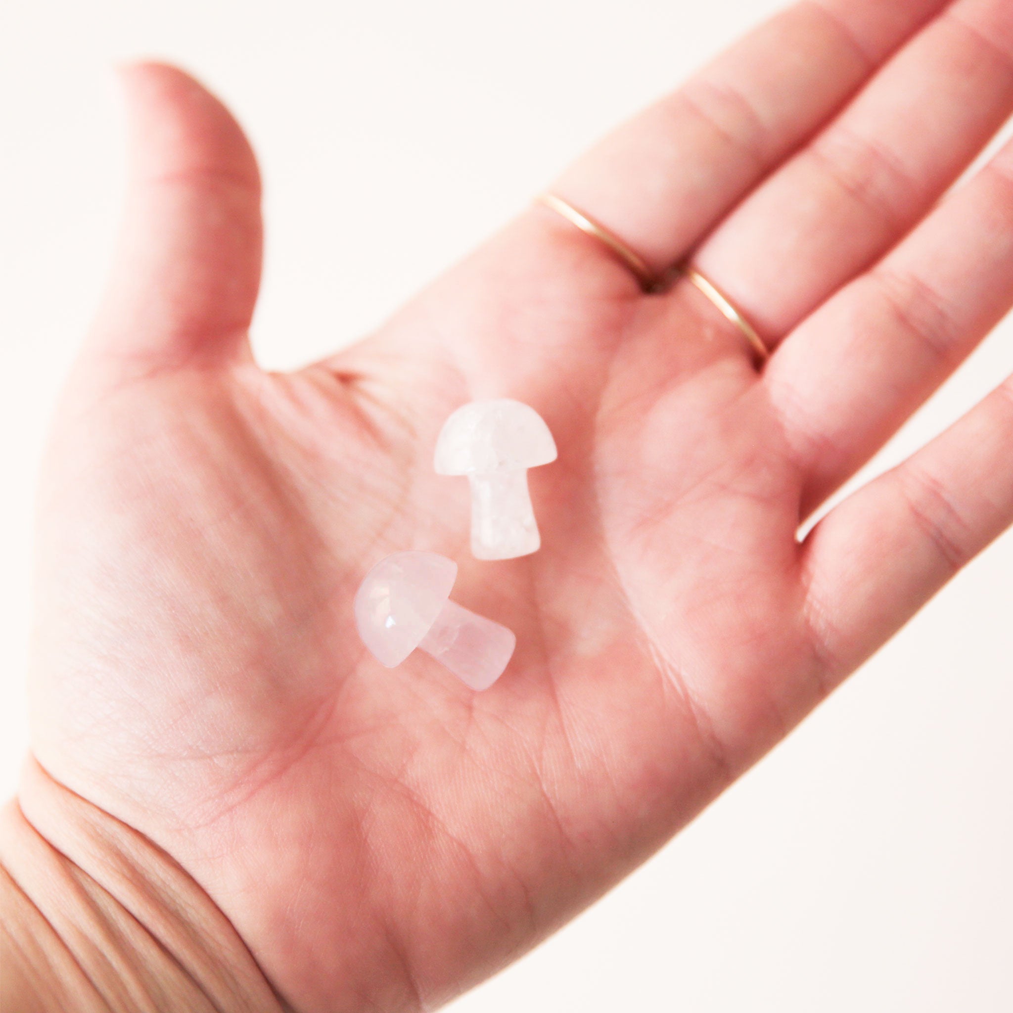 On a light gray background is a model holding two tiny mushroom shaped white quartz crystals. 