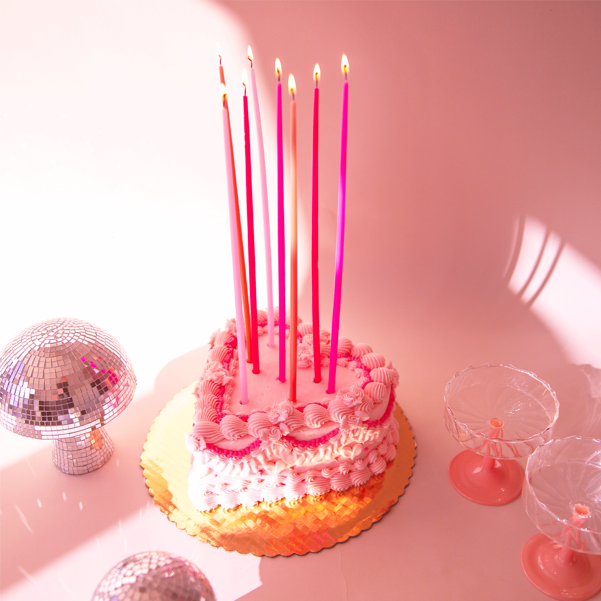 Super tall tapered candles in various shades of pink staged in a birthday cake.