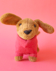 On a pink background is a tan sausage dog stuffed animal wearing a pink sweater.