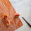 On a marble background is an orange kitchen towel with a white banana leaf design. 