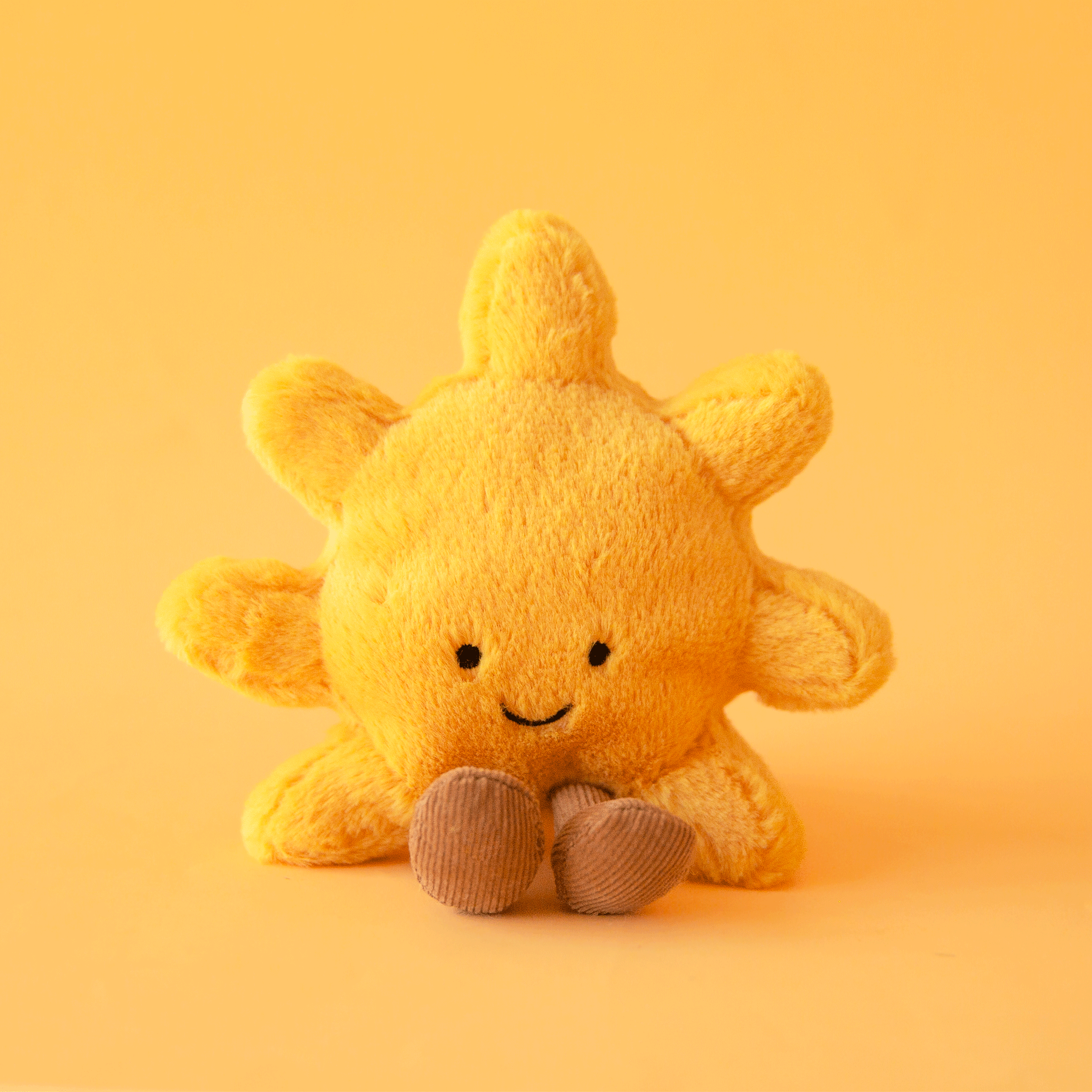 On a yellow background is a yellow sun shaped stuffed toy keychain / bag charm. 