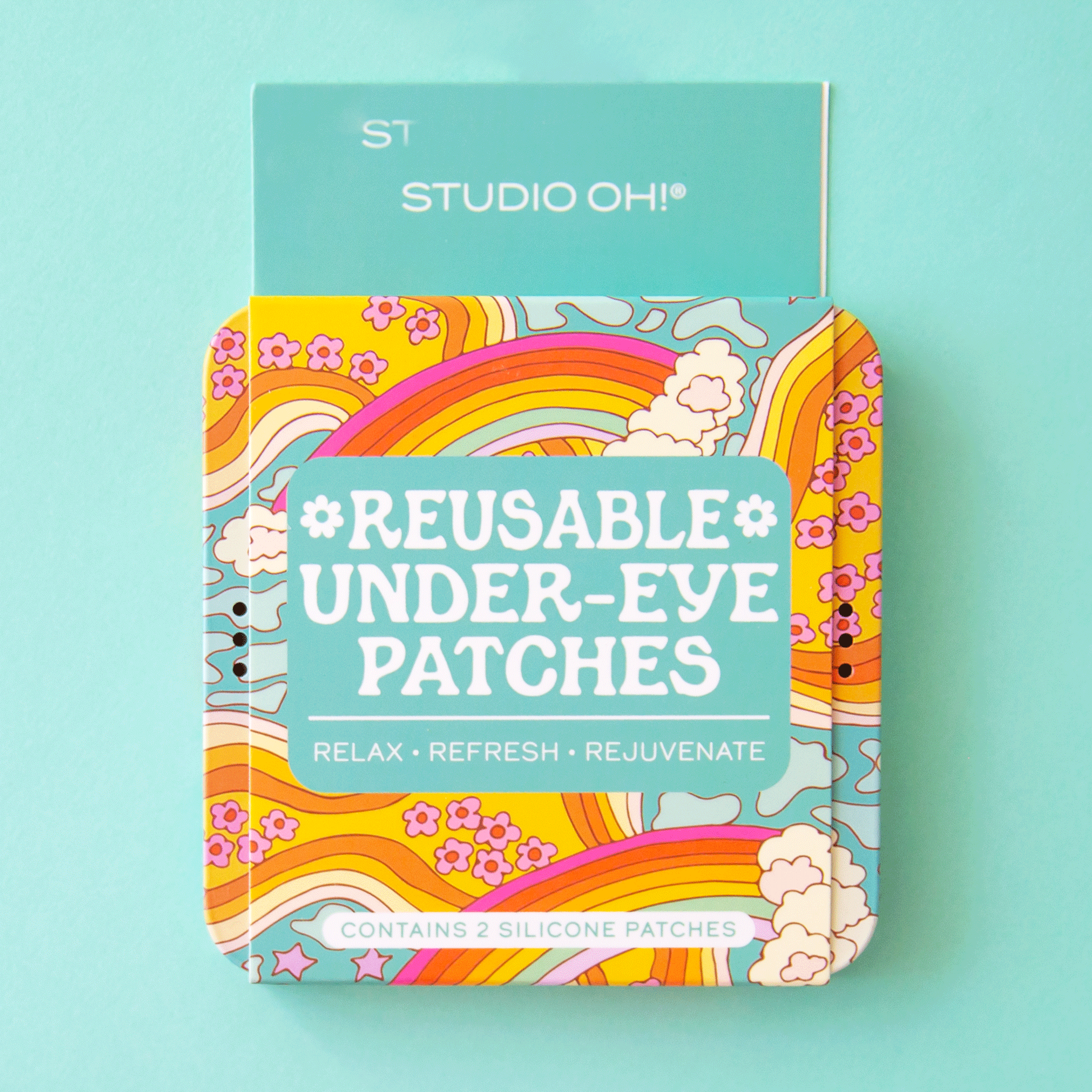 On a mint green background is a colorful rainbow packaging that holds one pair of green daisy printed reusable eye patches. 