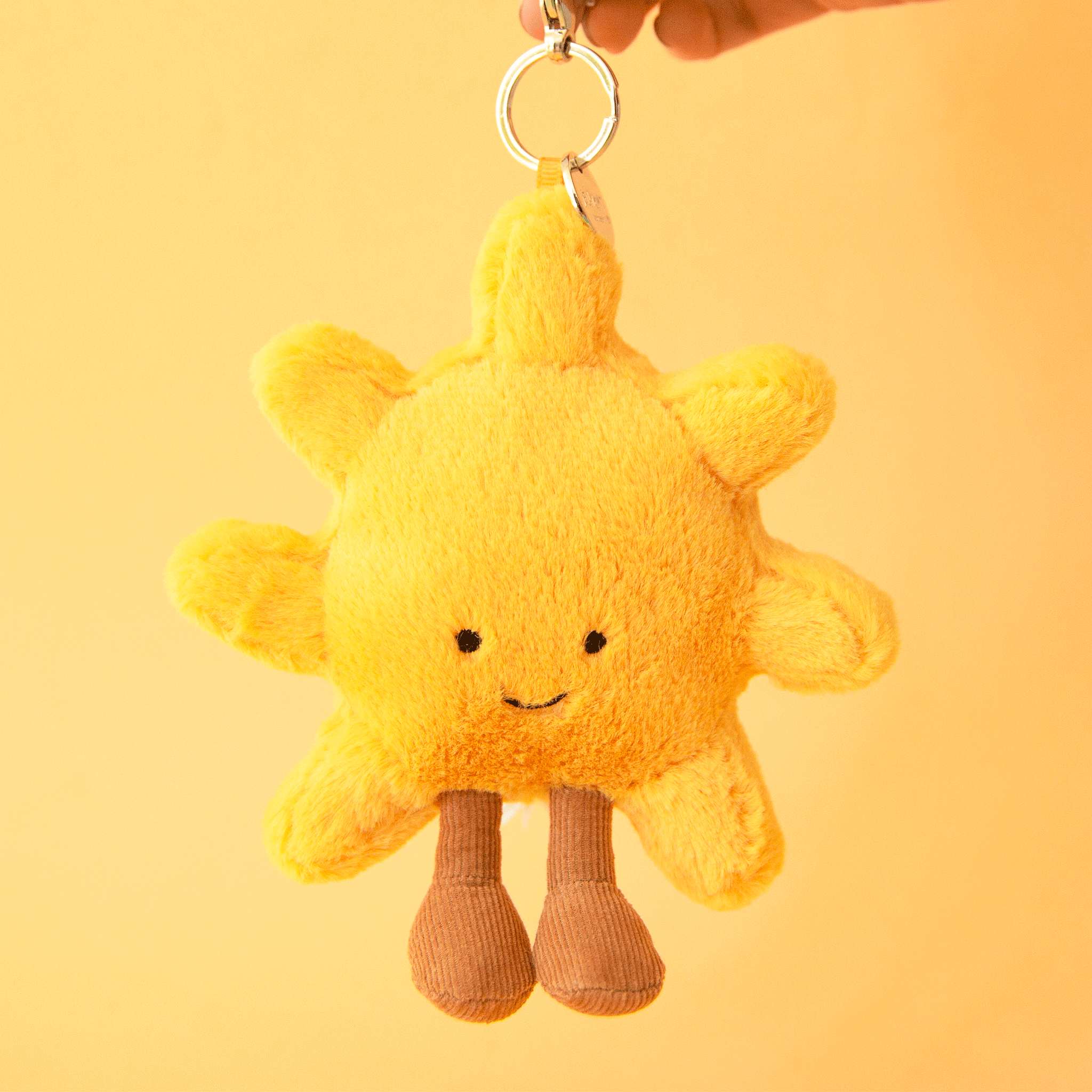 On a yellow background is a yellow sun shaped stuffed toy keychain / bag charm.