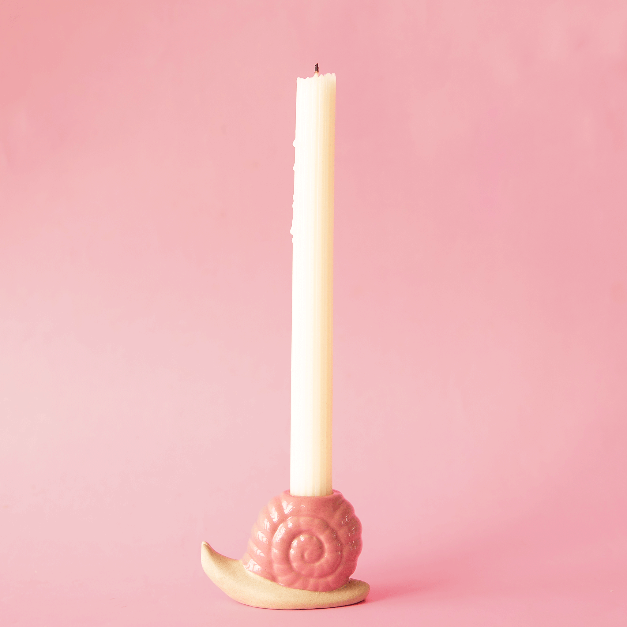 On a pink background is a ceramic pink snail shaped candle holder.