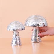 On a peach background is two different sized disco mushrooms with mirrored square pieces all over. 