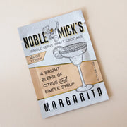 A tangerine and white packet of margarita mix with the title, "Noble Mick's Single Serve Craft Cocktails" along with a drawing of a margarita and their mascot which is a moose