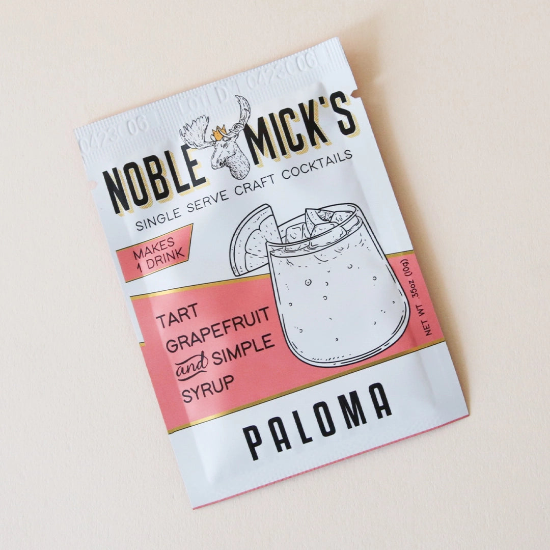 A pink and white packet of cocktail mix that reads, &quot;Noble Mick&#39;s Single Serve Cocktails&quot; along with an illustration of a paloma with its signature grapefruit garnish.