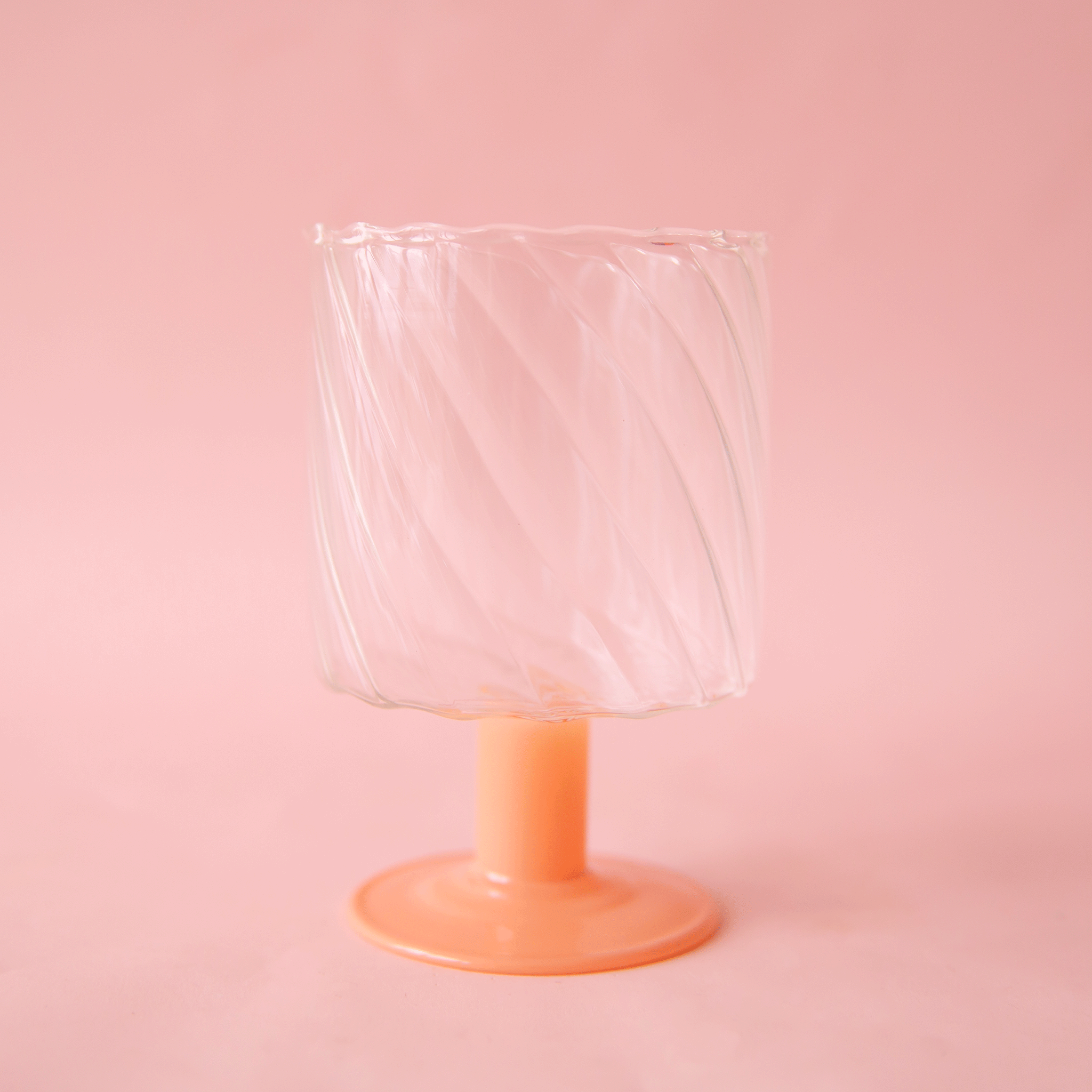 A wavy glass wine glass with a pink short stem. 