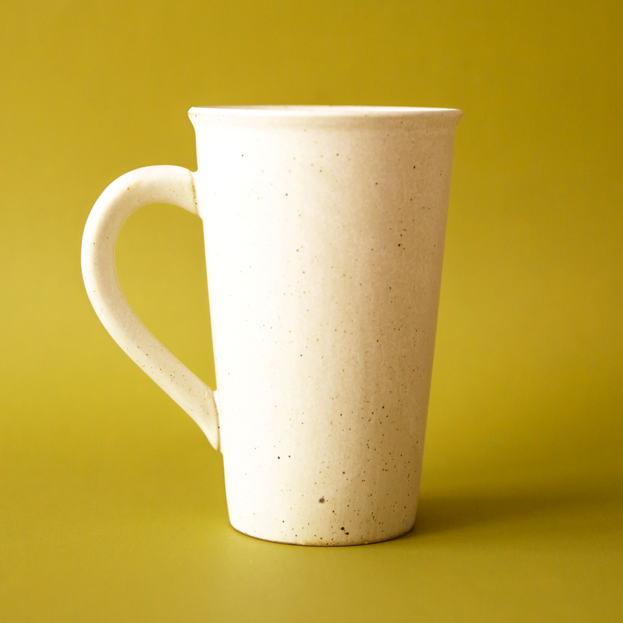 On a green background is a white stoneware mug. 