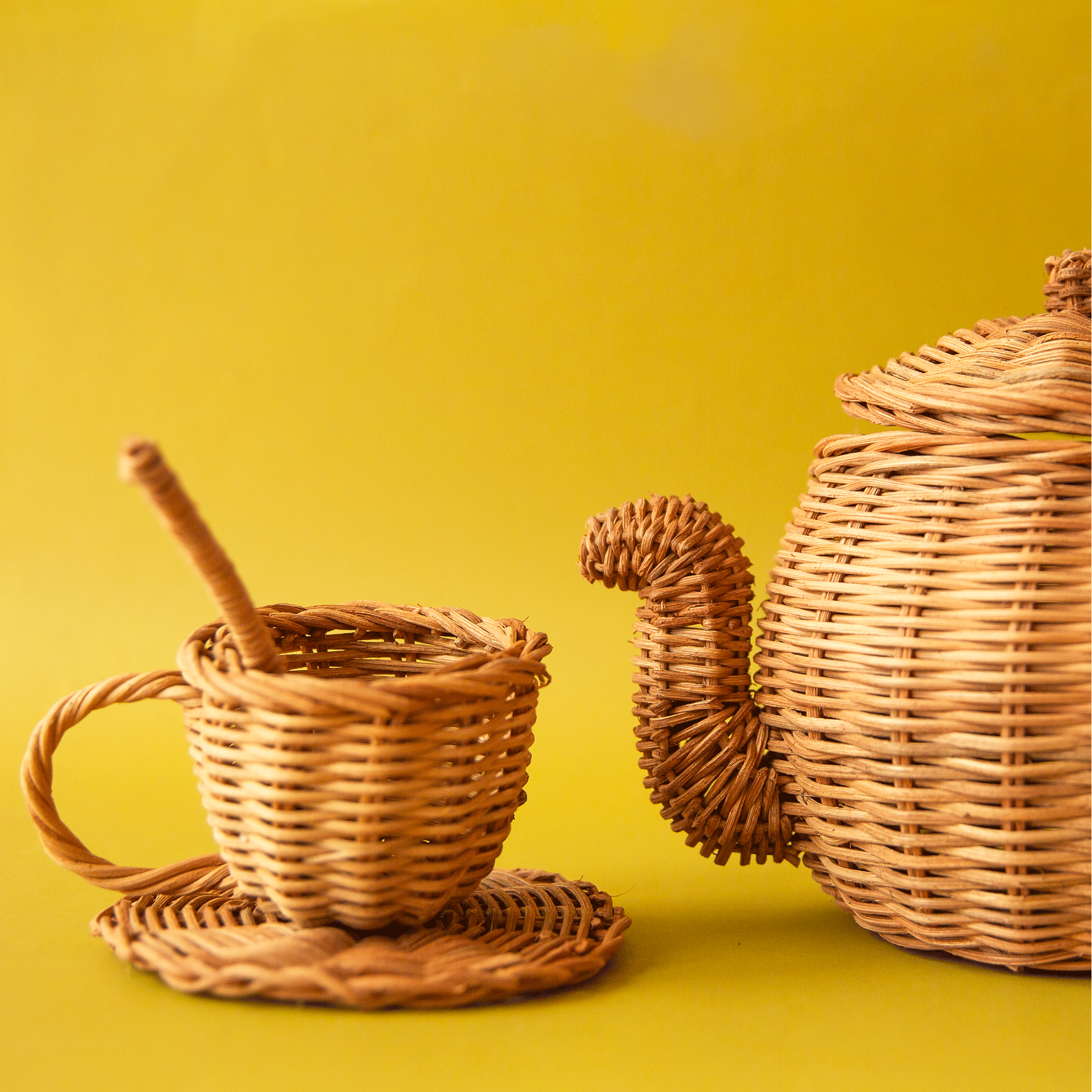 On a chartreuse background is a rattan tea pot and rattan tea cup, saucer and spoon. 