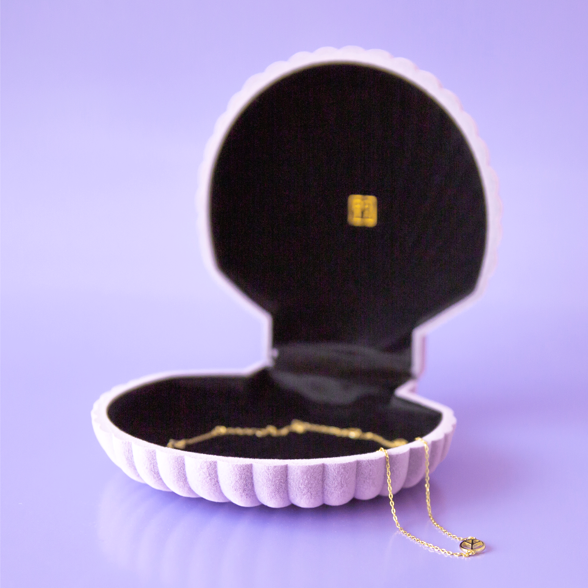 On a purple background is a purple velvet seashell shaped jewelry box with a necklace inside that is not included with purchase. 