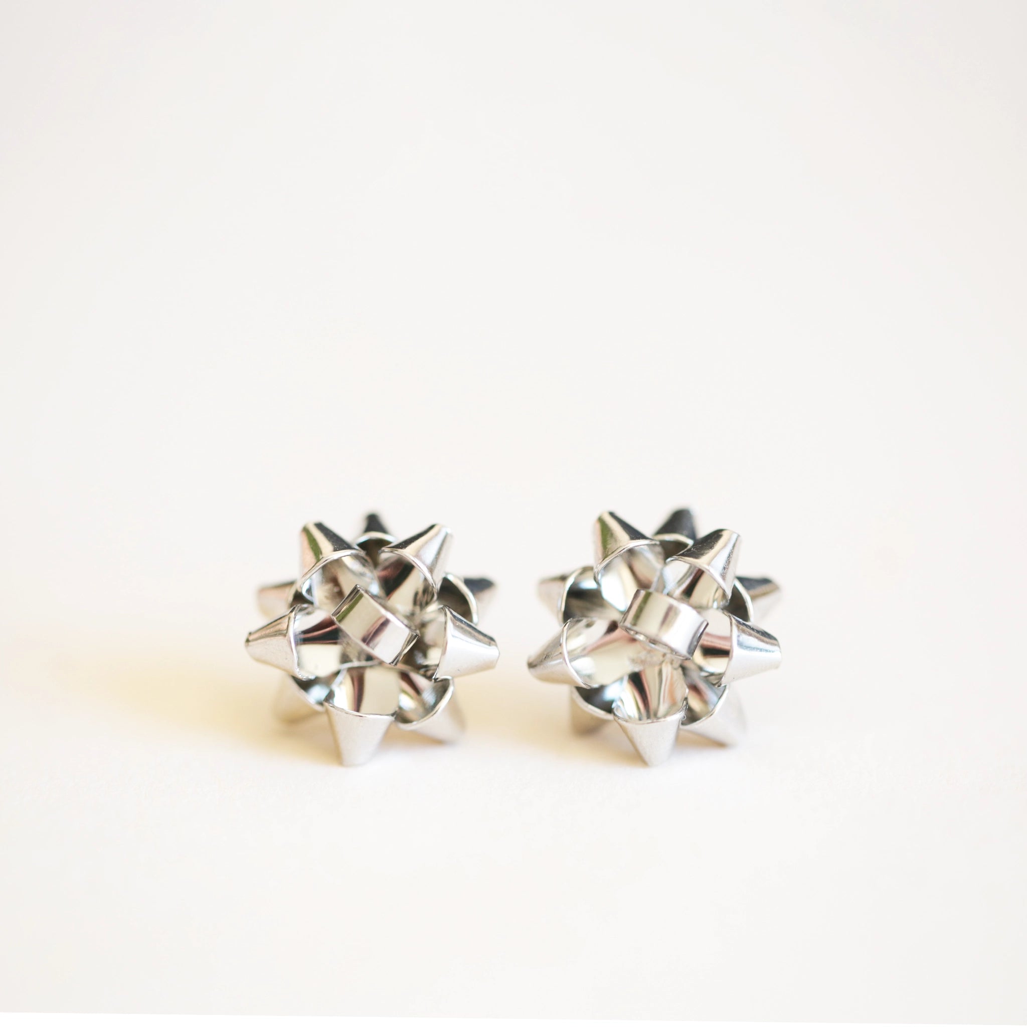 On an ivory background is a pair of silver earrings in the shape of holiday bows.