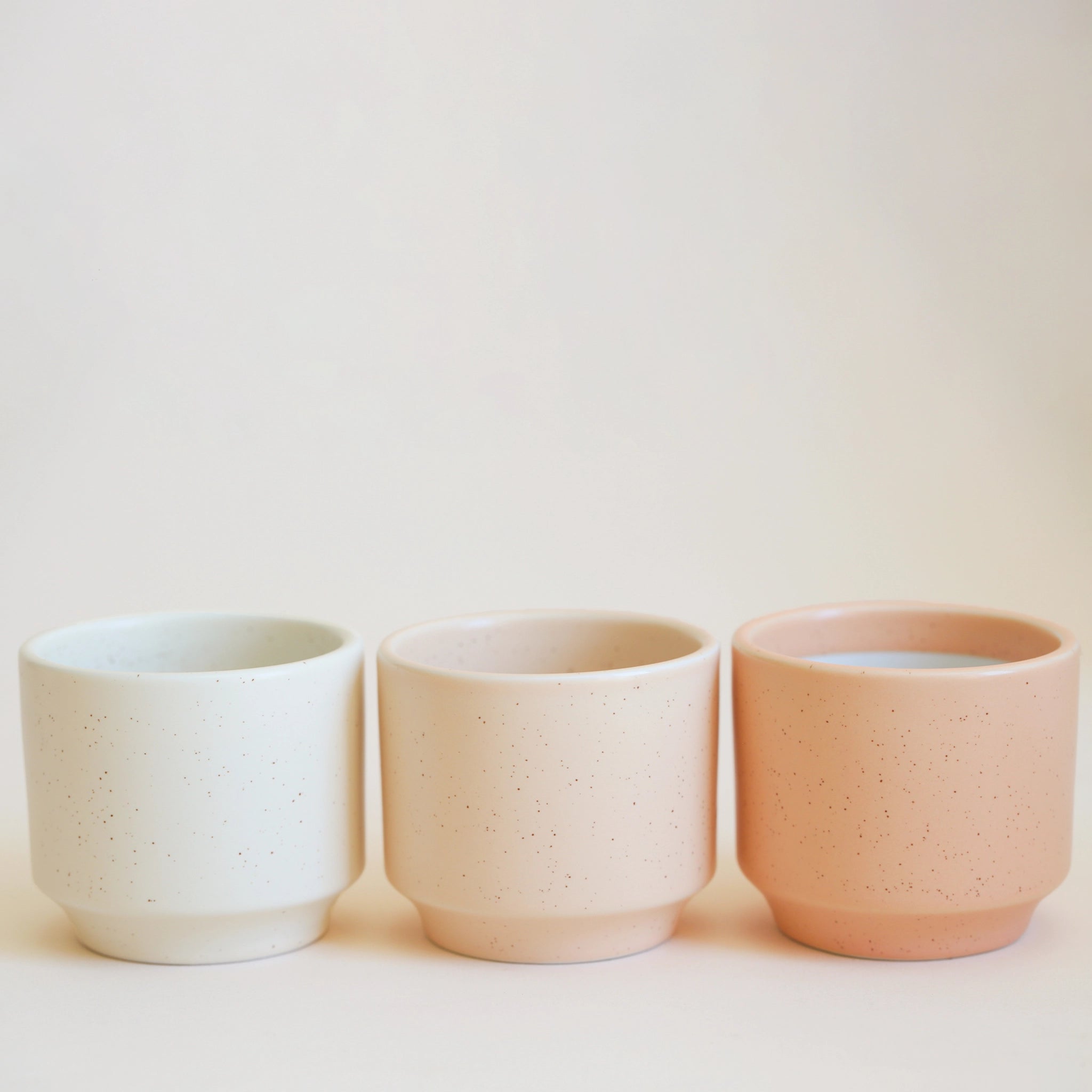 On an ivory background is three ceramic planters in different colors. From left to right the colors are Vintage White, Vanilla, and Sunset.
