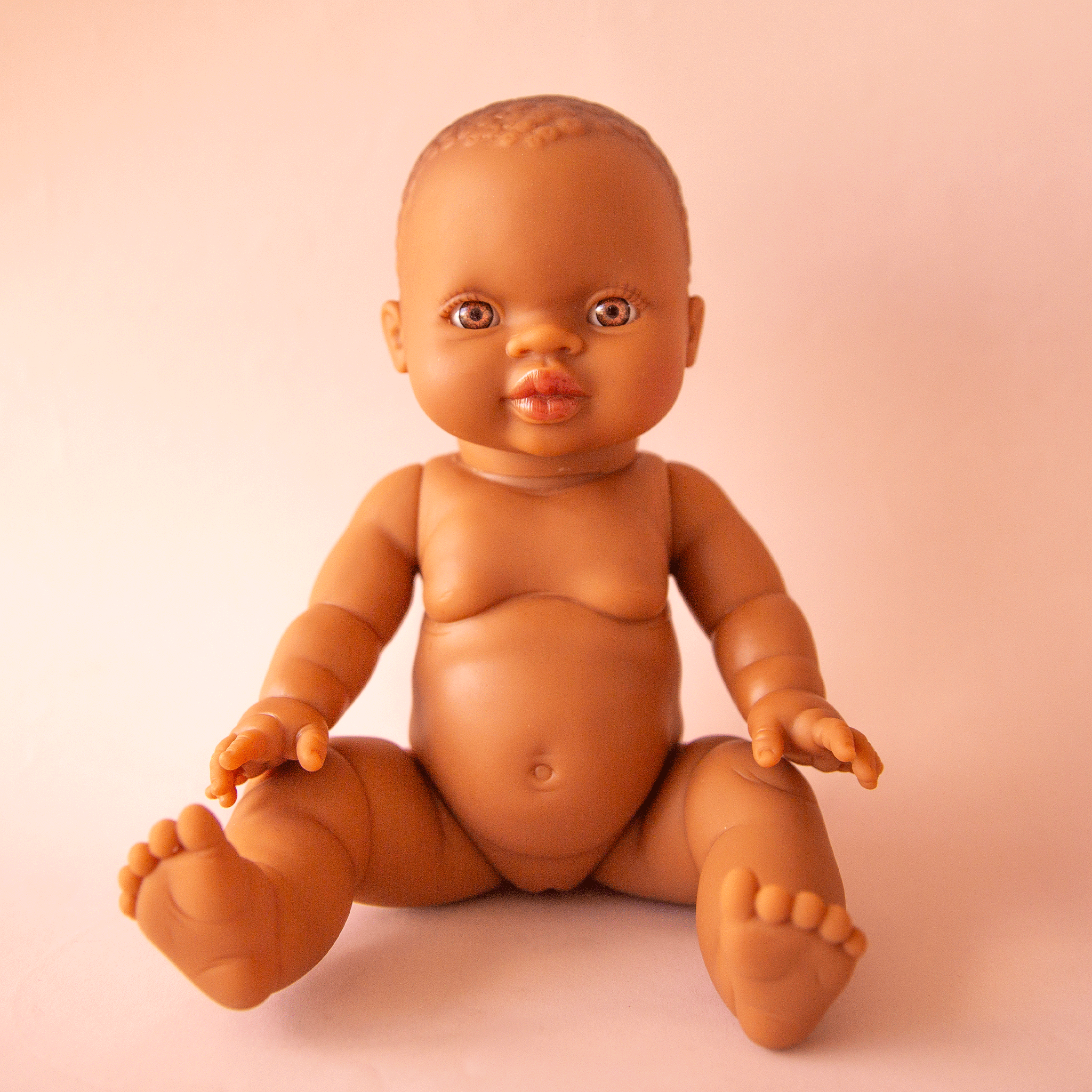 An African American baby girl doll photographed in front of a cream background.