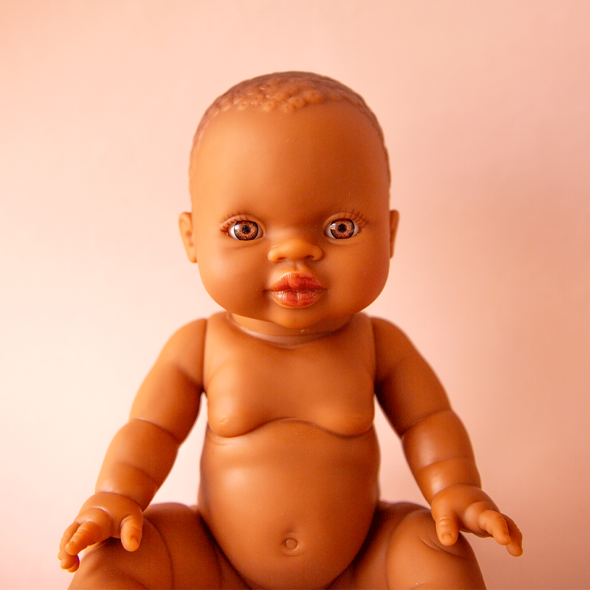 An African American baby girl doll photographed in front of a cream background.