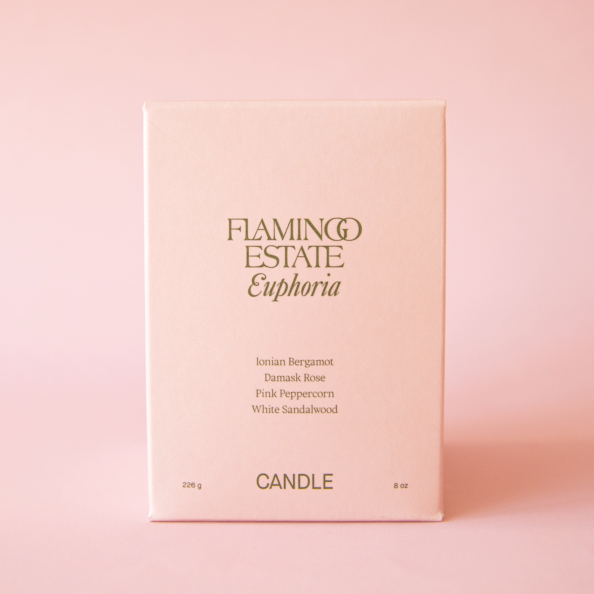 On a pink background is a light tan / pink box filled with a candle and text on the front that reads, "Flamingo Estate Euphoria Candle". 