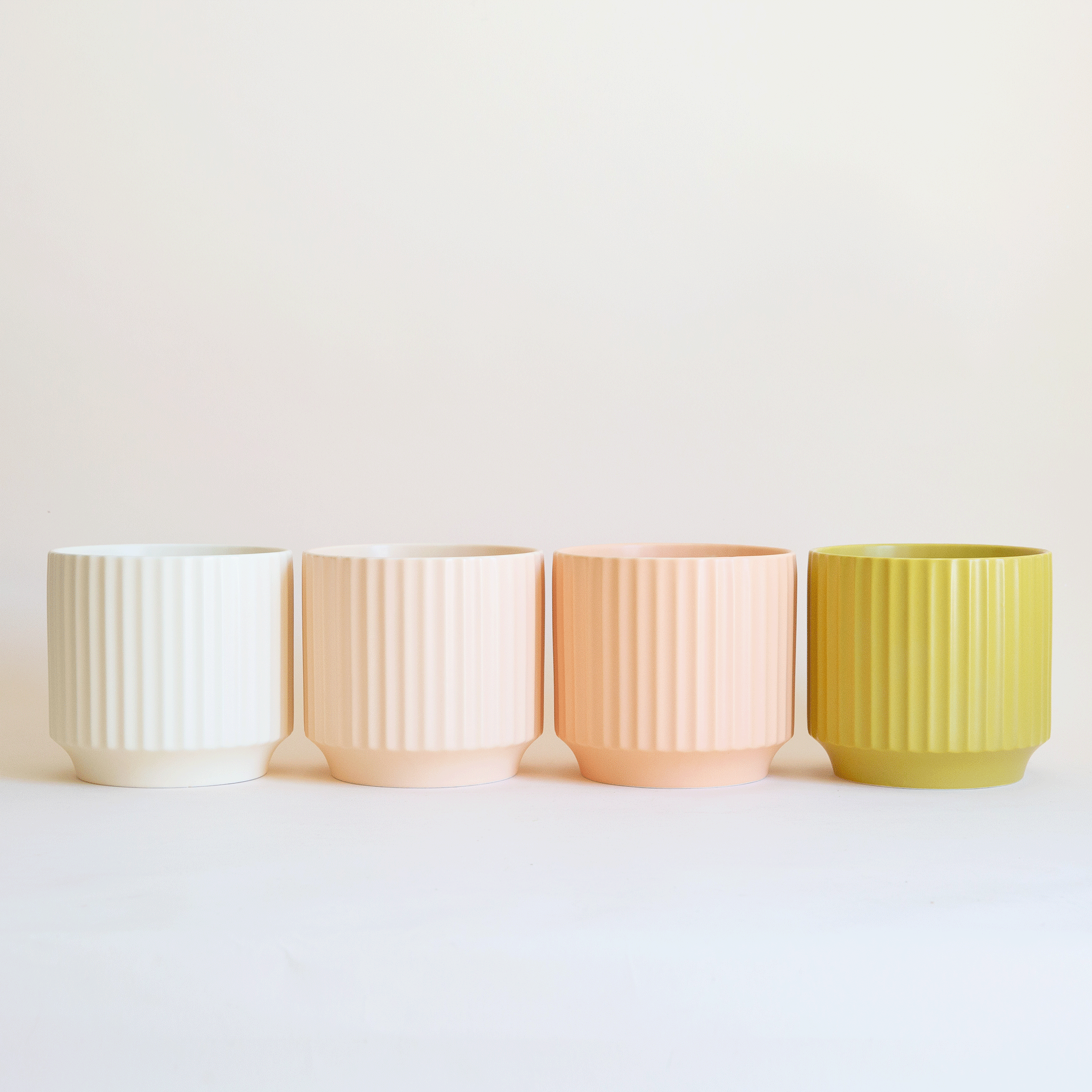 On a white background is four ceramic planters in four shades ranging from ivory to pinks to chartreuse.
