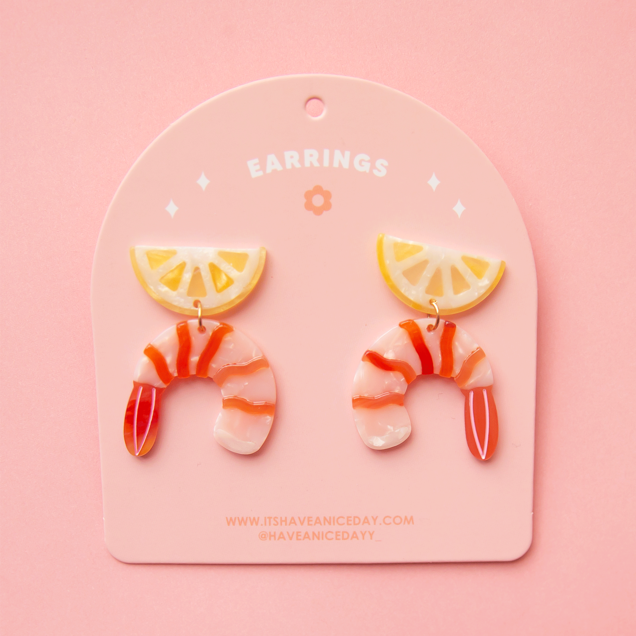 On a pink background is a pair of shrimp cocktail and lemon shaped acetate earrings with a straight back post.