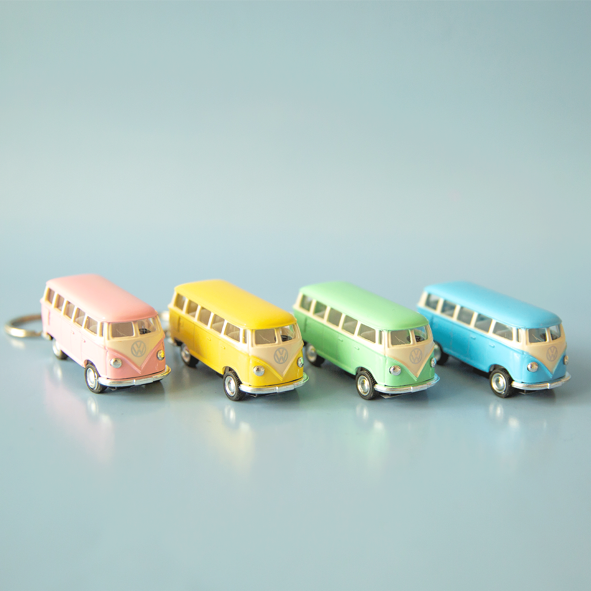 On a blue background is four VW bus shaped keychains in pink, yellow, green and blue. Each color sold separately.