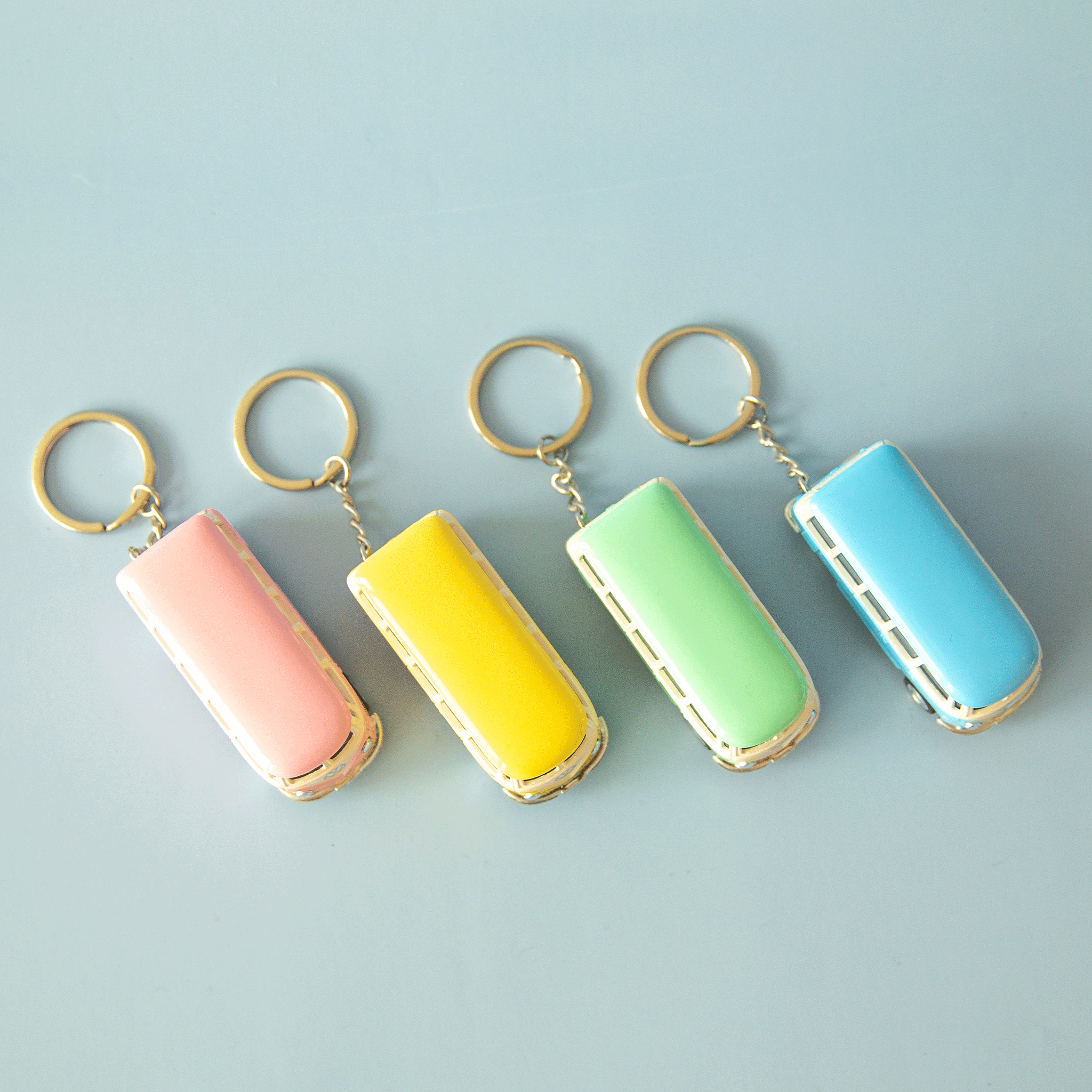 On a blue background is four VW bus shaped keychains in pink, yellow, green and blue. Each color sold separately.