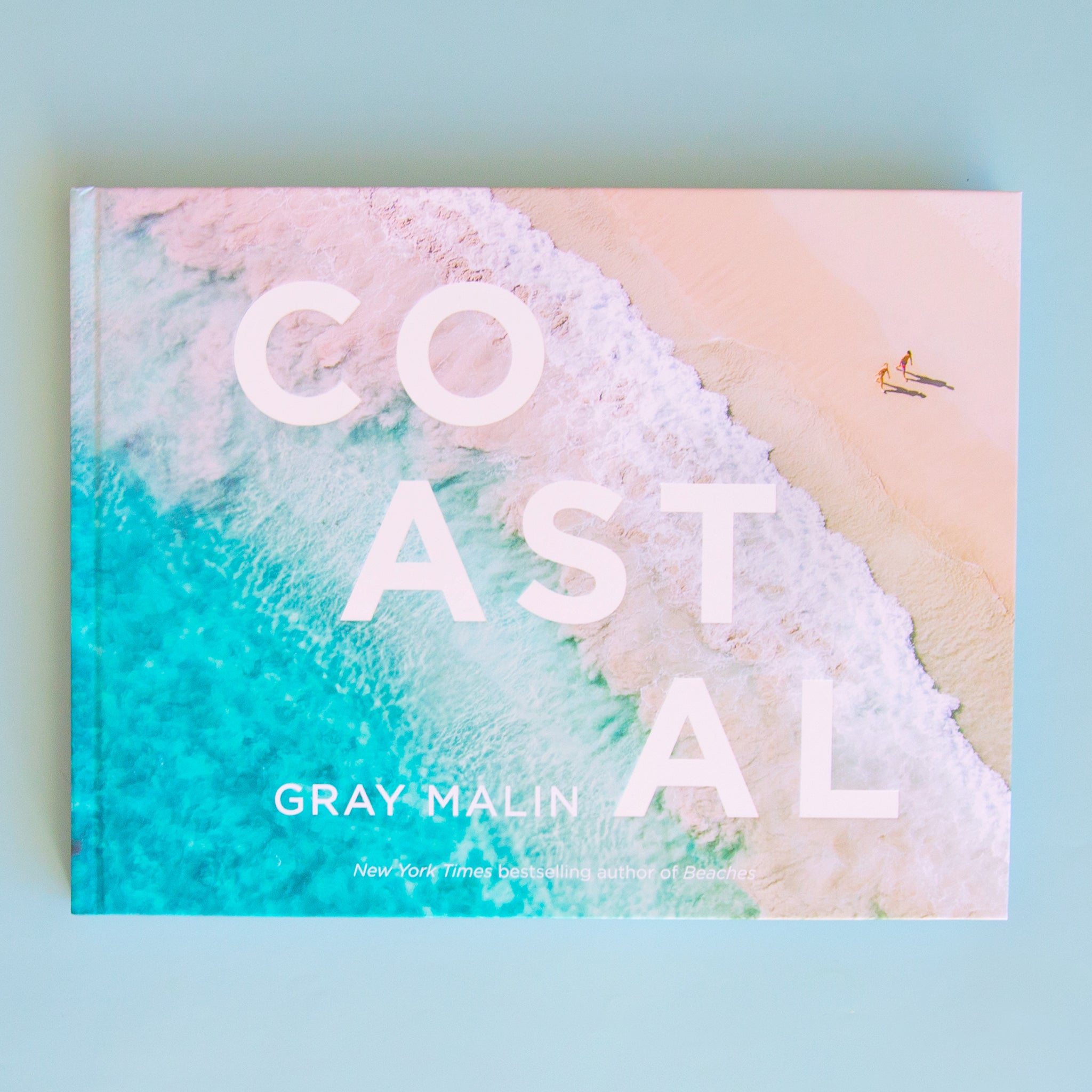 On a blue background is a Gray Malin book cover with one of his ocean photography shots as well as white text that reads, "COASTAL".
