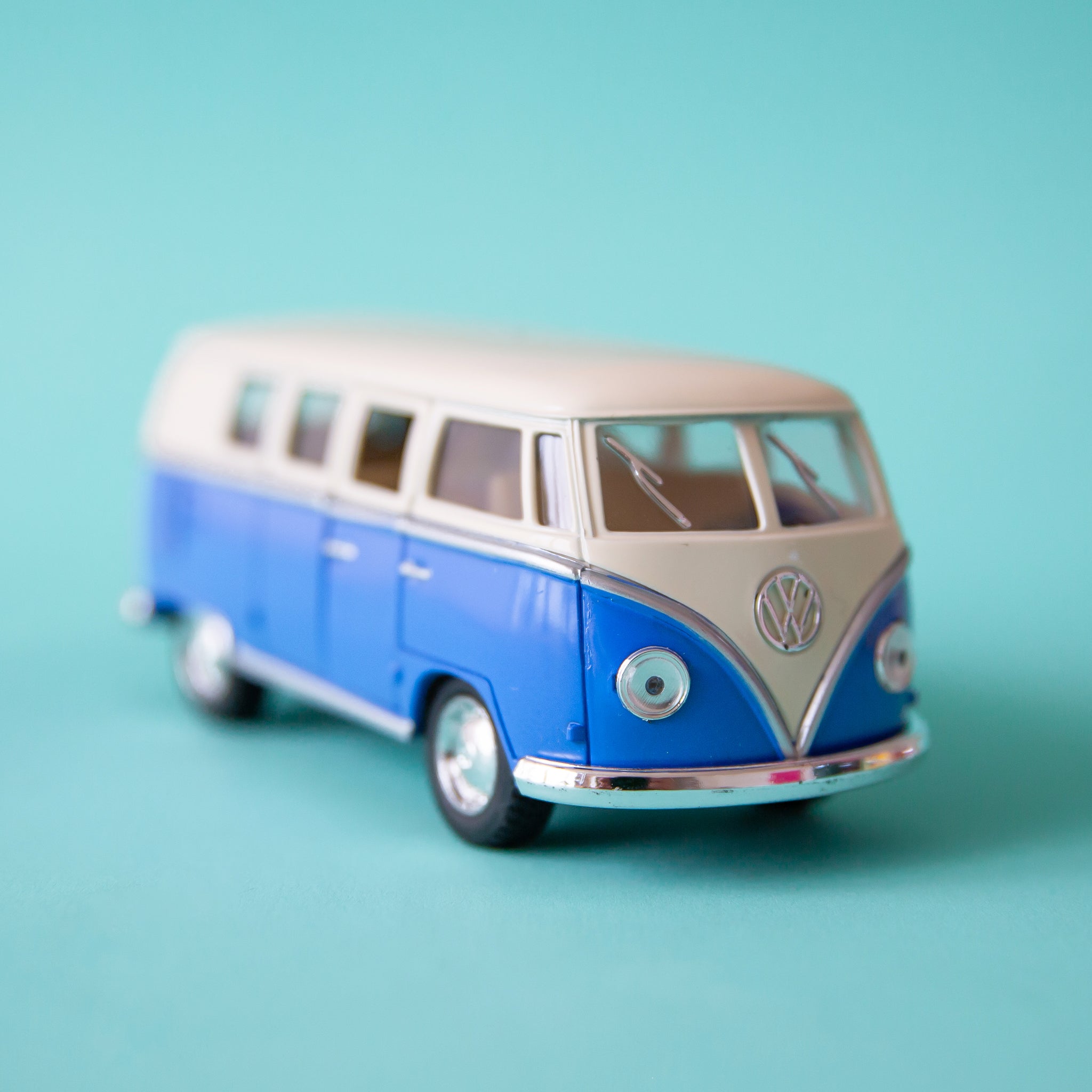 On a blue background is a blue and white VW bus toy. 