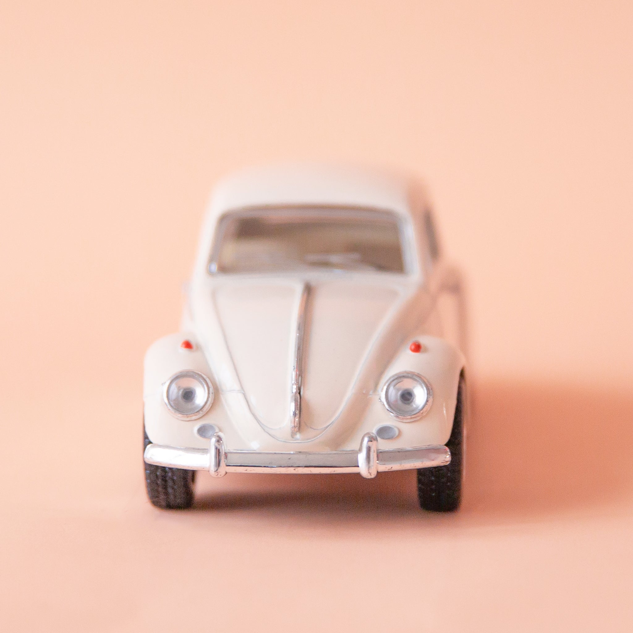 On a tan background is a white beetle toy car.