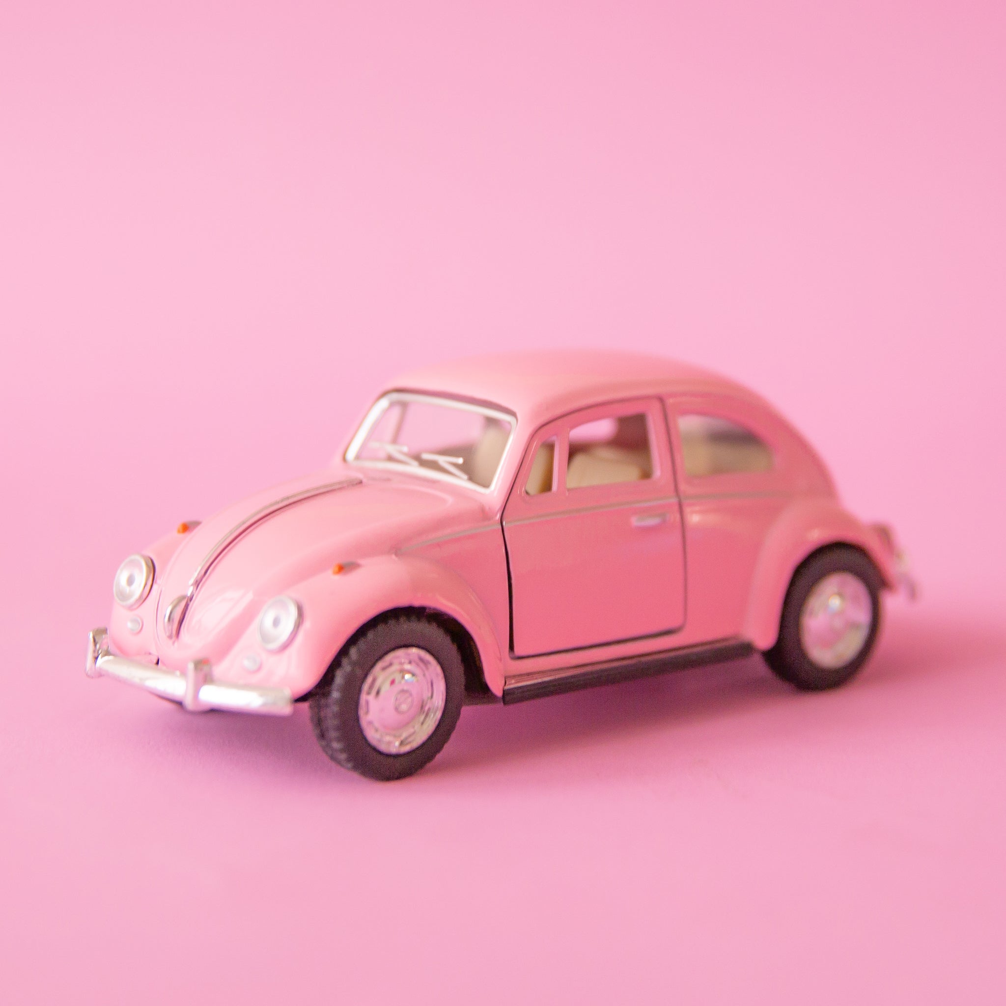 On a pink background is a pink beetle car toy. 